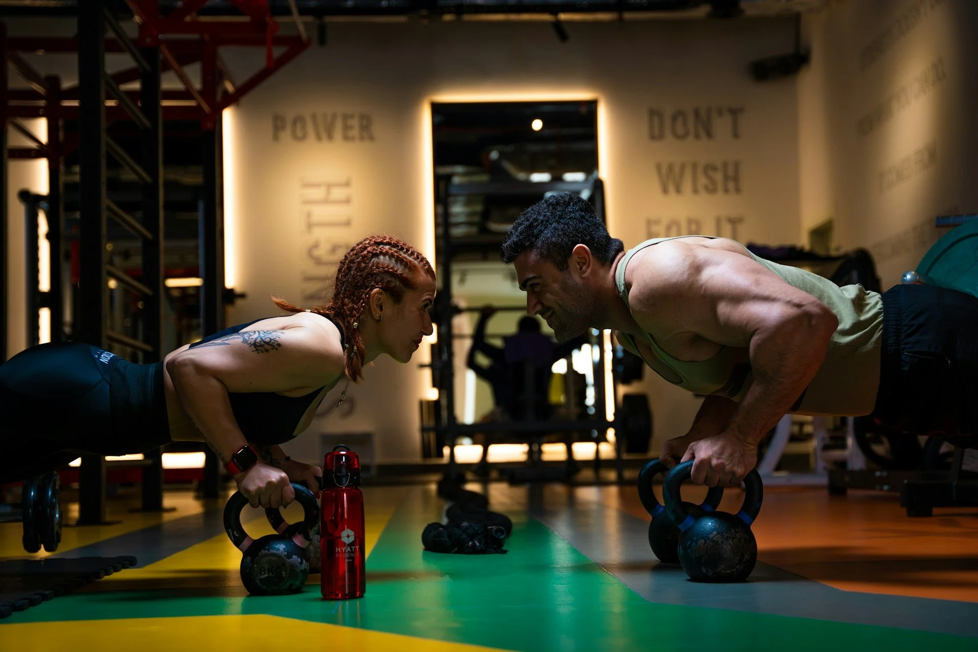 Two people performing kettlebell renegade rows during a strength workout at the gym.