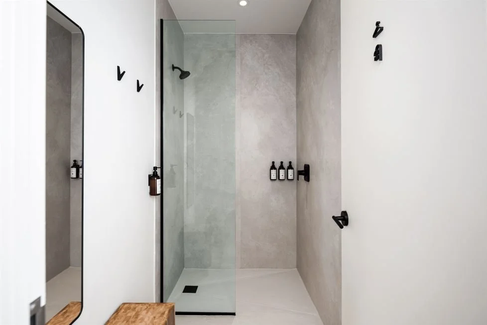 Modern spa shower with a glass door, black fixtures, and minimal decor in white and gray tones.