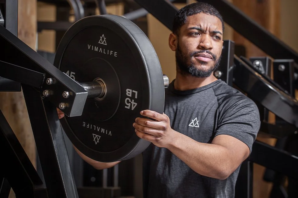 A man lifting a 45-pound weight plate on a workout machine in a gym.