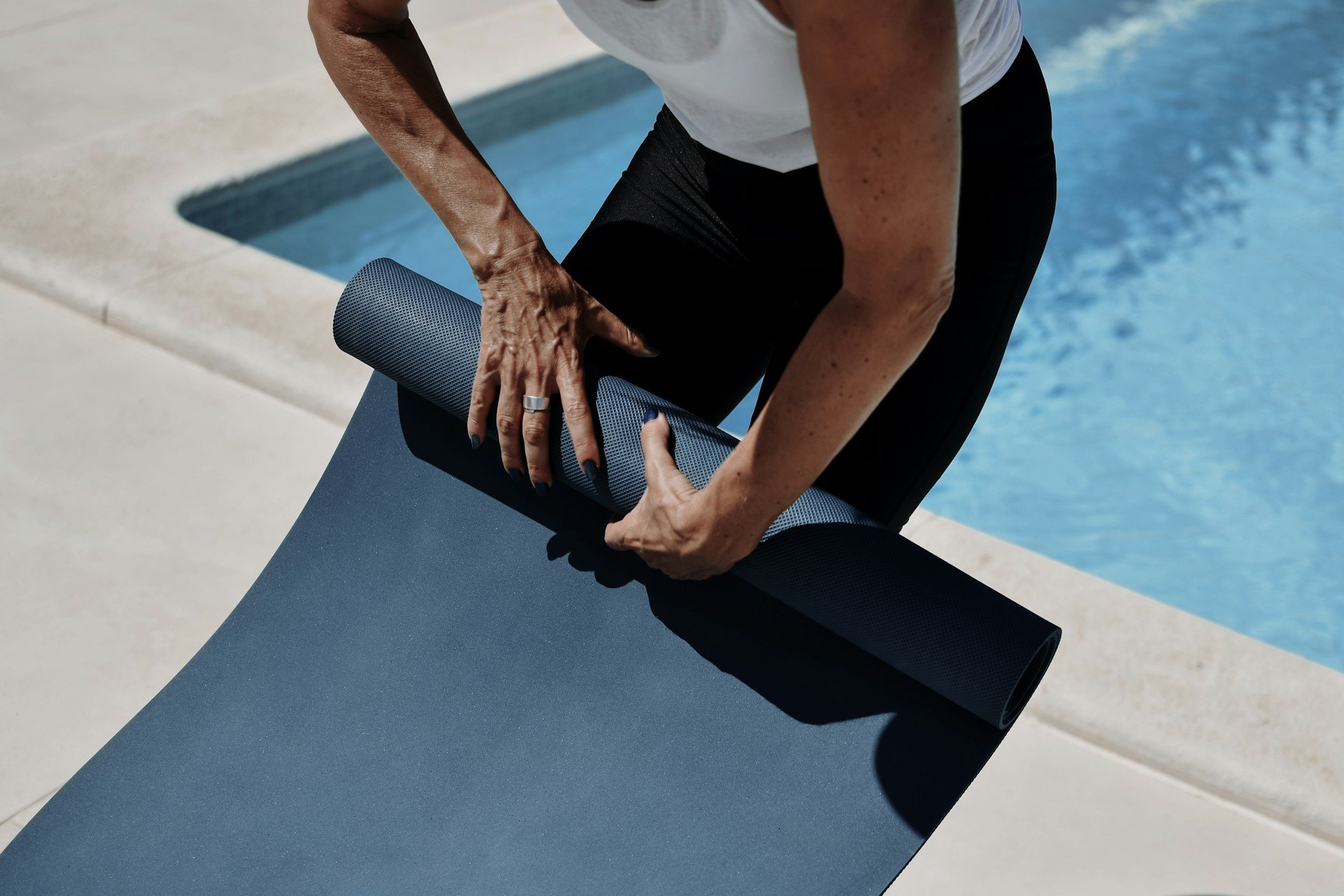 Person rolling out a yoga mat beside a pool for a wellness or recovery session.