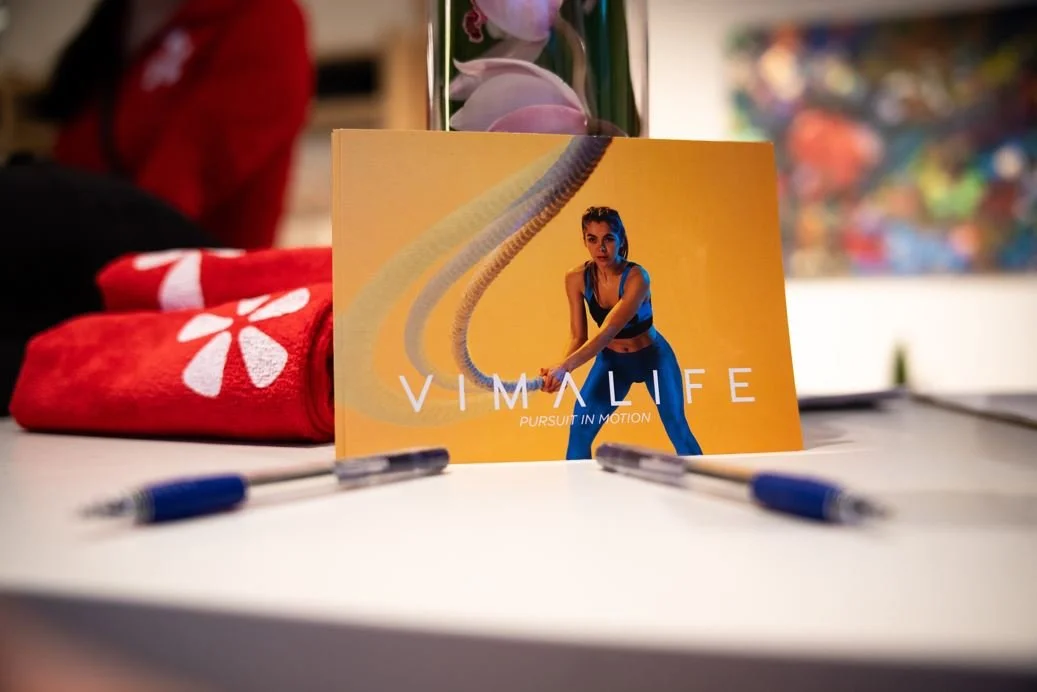 A colorful promotional display featuring a woman in athletic clothing on a yellow background with the text 'VIVALLIFE' and 'PURSUIT IN MOTION'.