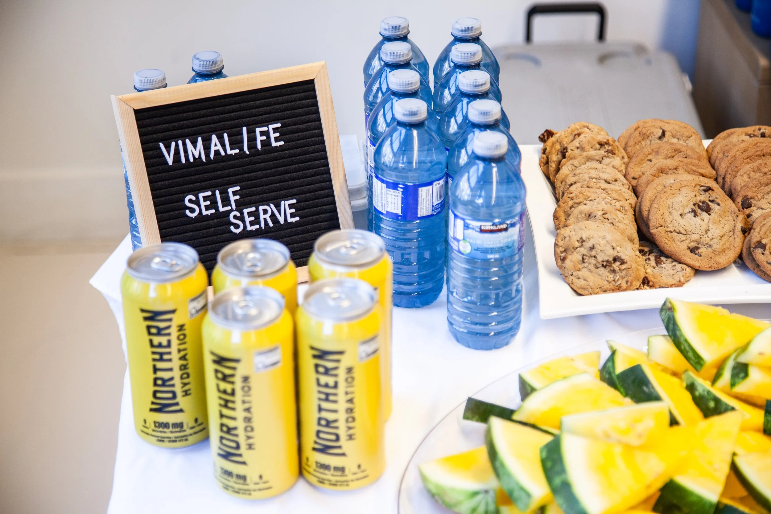 VIMALIFE self-serve refreshment table with water, hydration drinks, cookies and fruit.