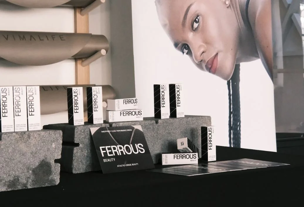Display of Ferrous Beauty products arranged on gray stone blocks and a table, with a large poster of a woman with braided hair in the background.