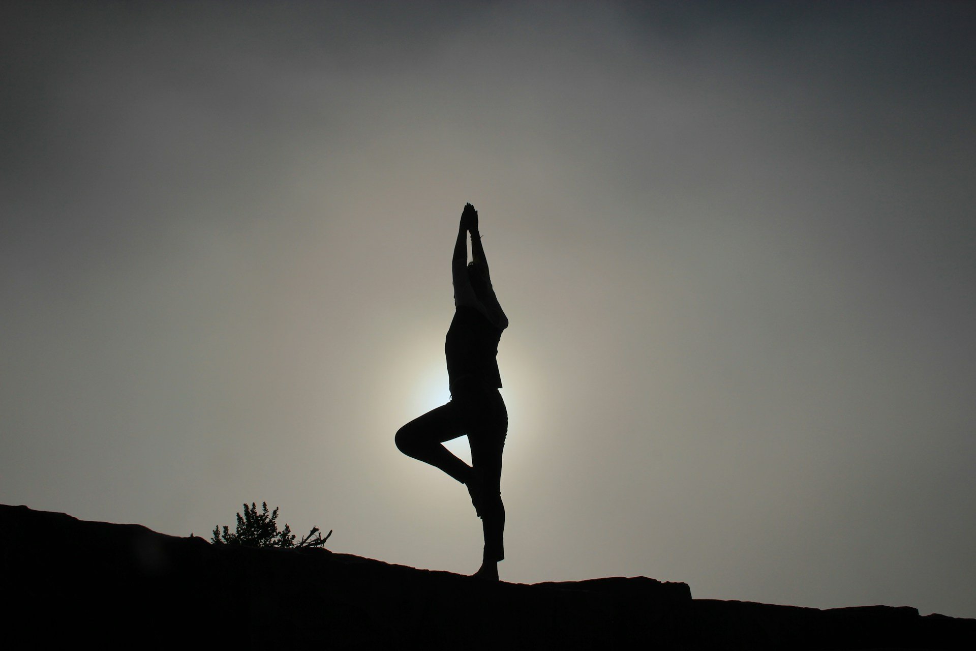 Silhouette of a person practicing tree pose yoga outdoors at sunset.