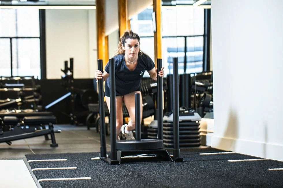 Woman pushing a weighted sled at VIMALIFE, highlighting strength training, conditioning and functional fitness in Leslieville.