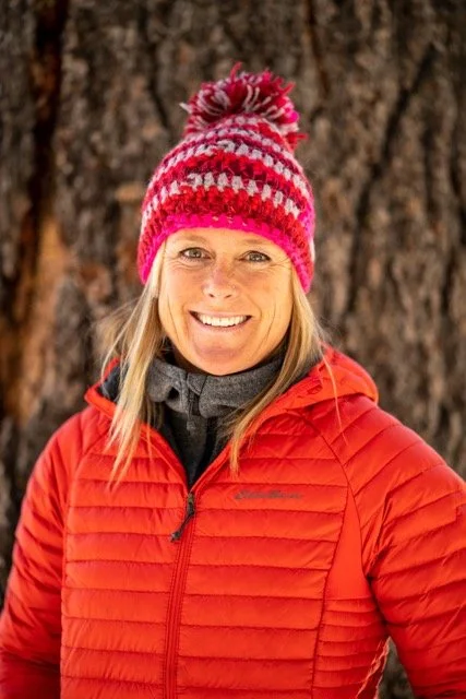 woman in pink beanie and red coat standing in front of a large tree