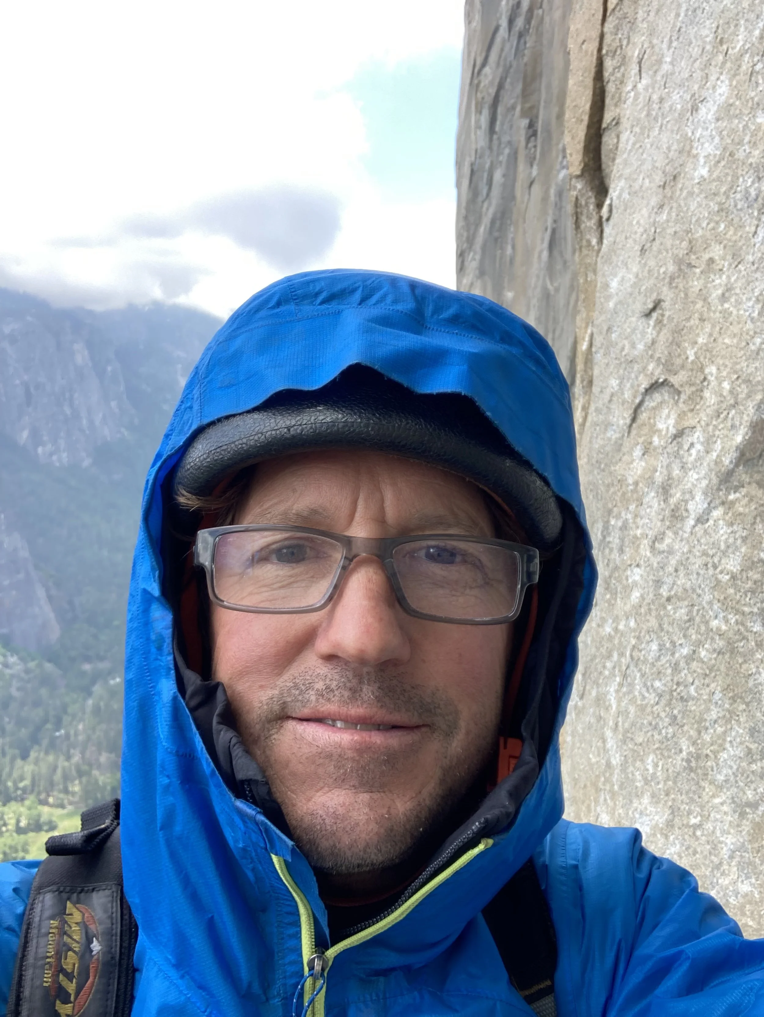 man with glasses with a blue hood, taken outside