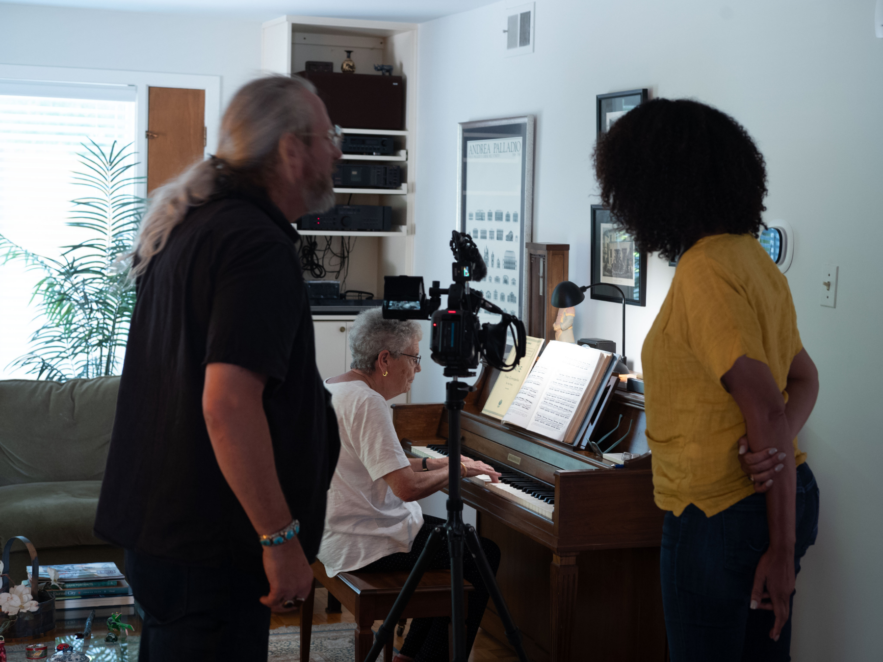 A woman playing a piano while two people film her indoors.