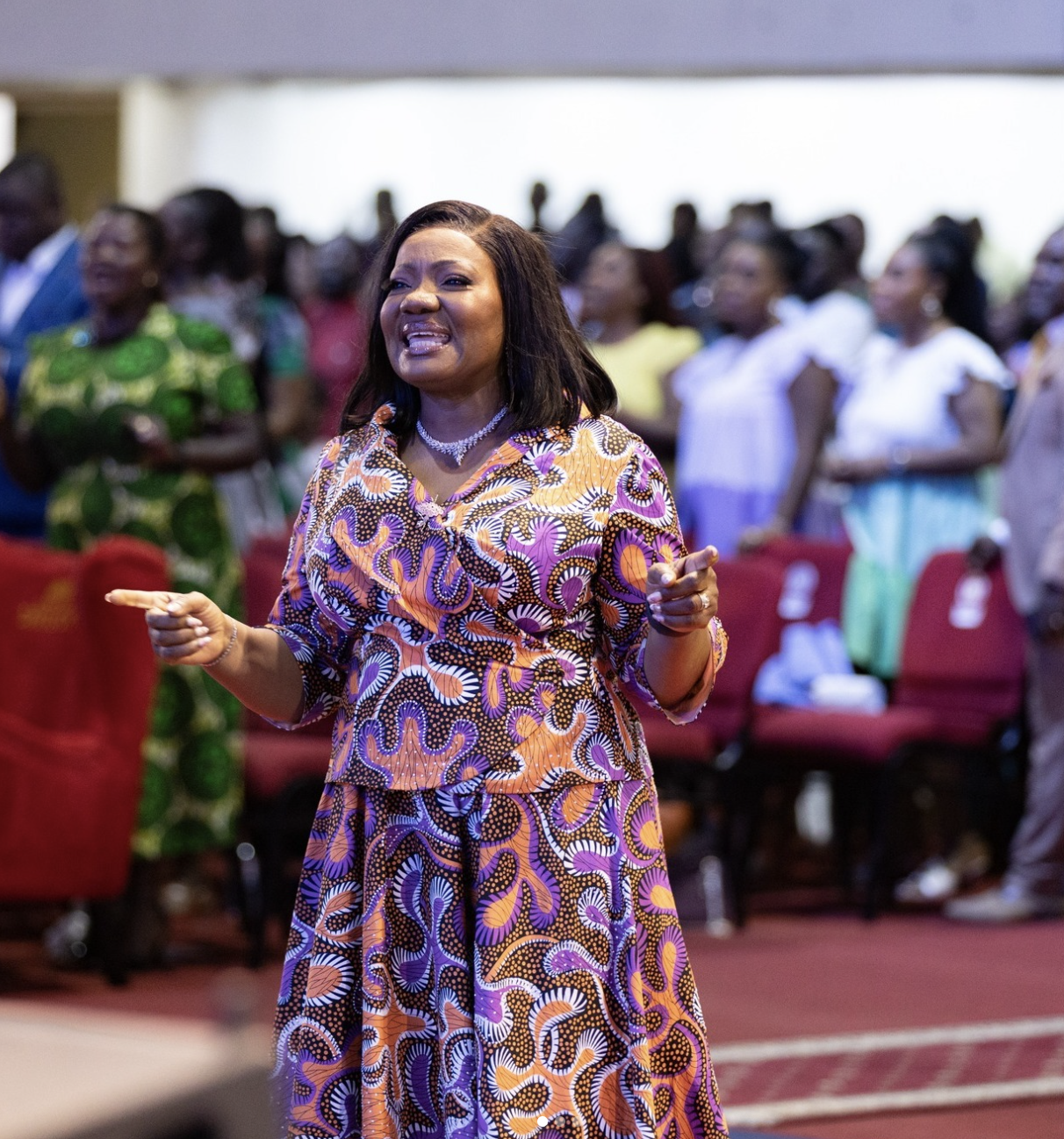 Our Premier Lady in colorful patterned dress praying and singing with the church congregation in the Oil Dome.