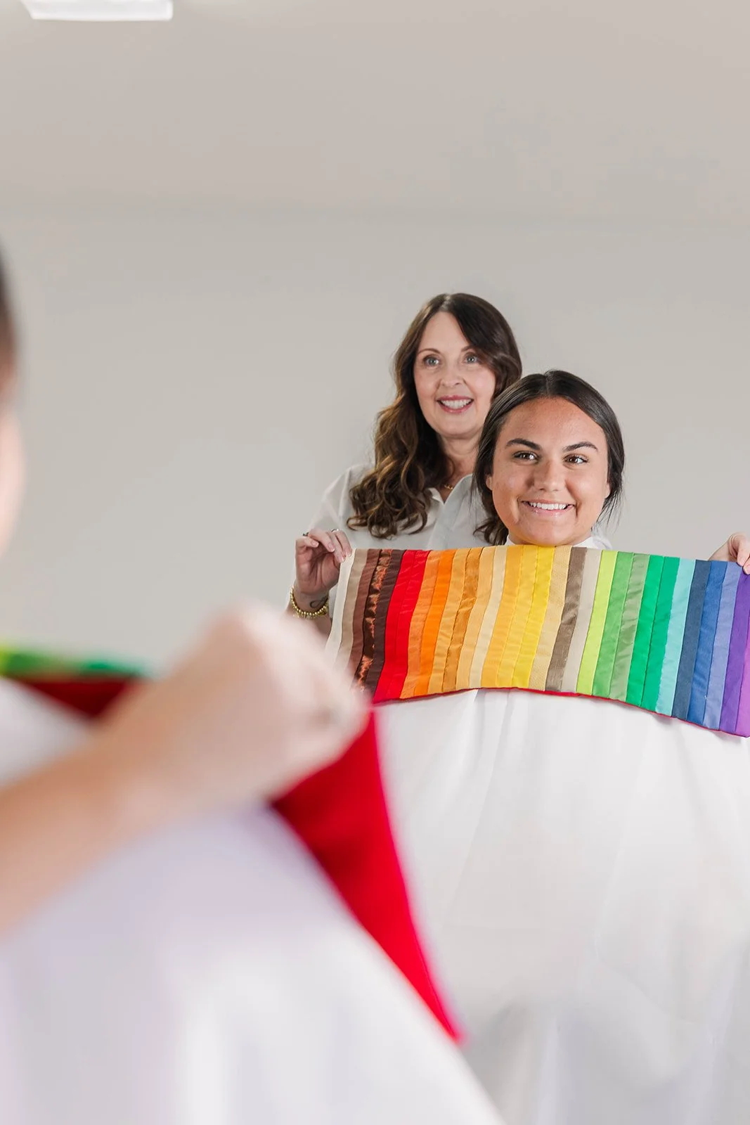 Young woman and older woman holding a rainbow-colored fabric while looking at a person with a rainbow-colored umbrella during a photo shoot.