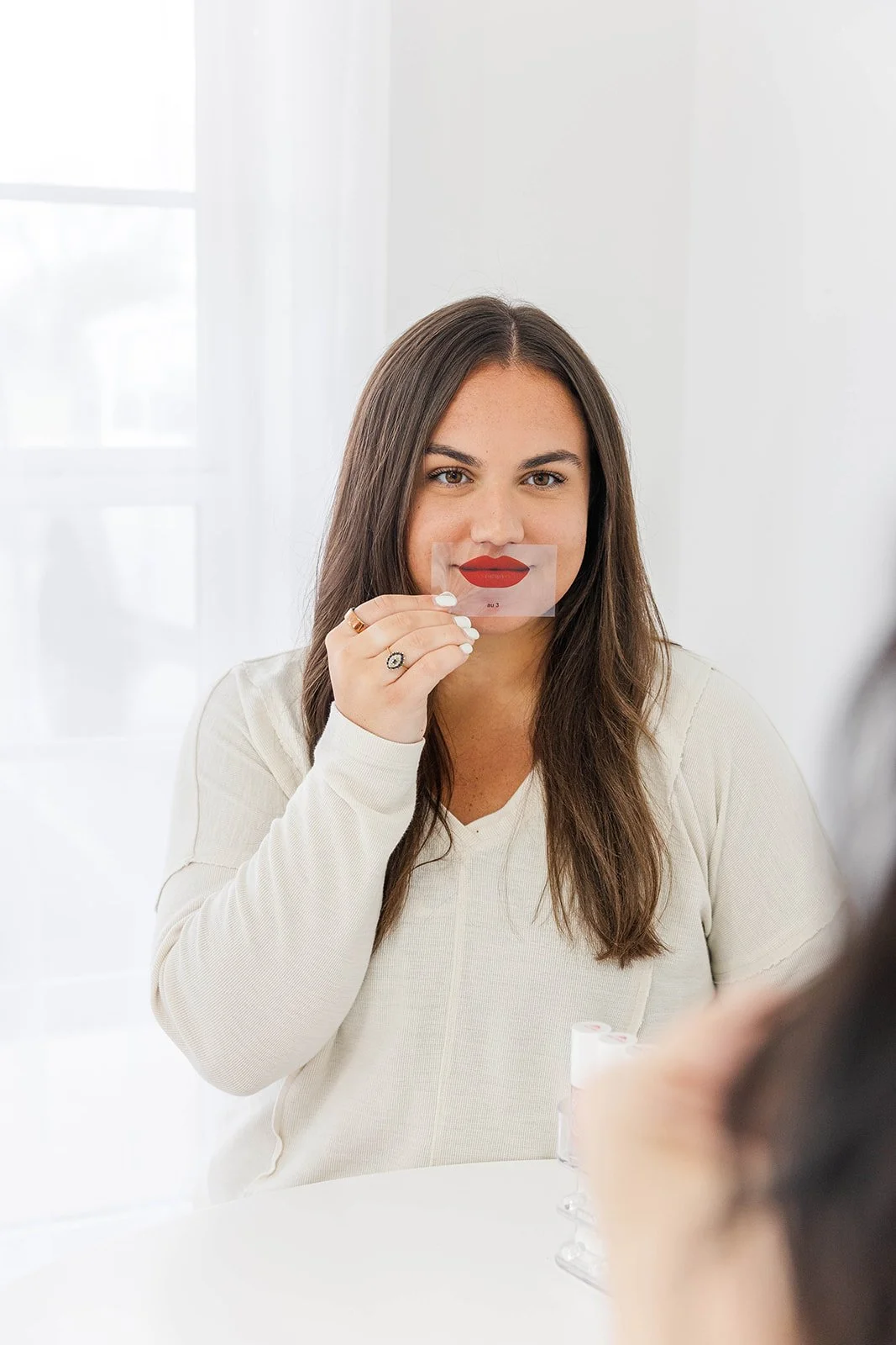 A woman holding a plastic lip test swatch in front of her face at a beauty consultation.