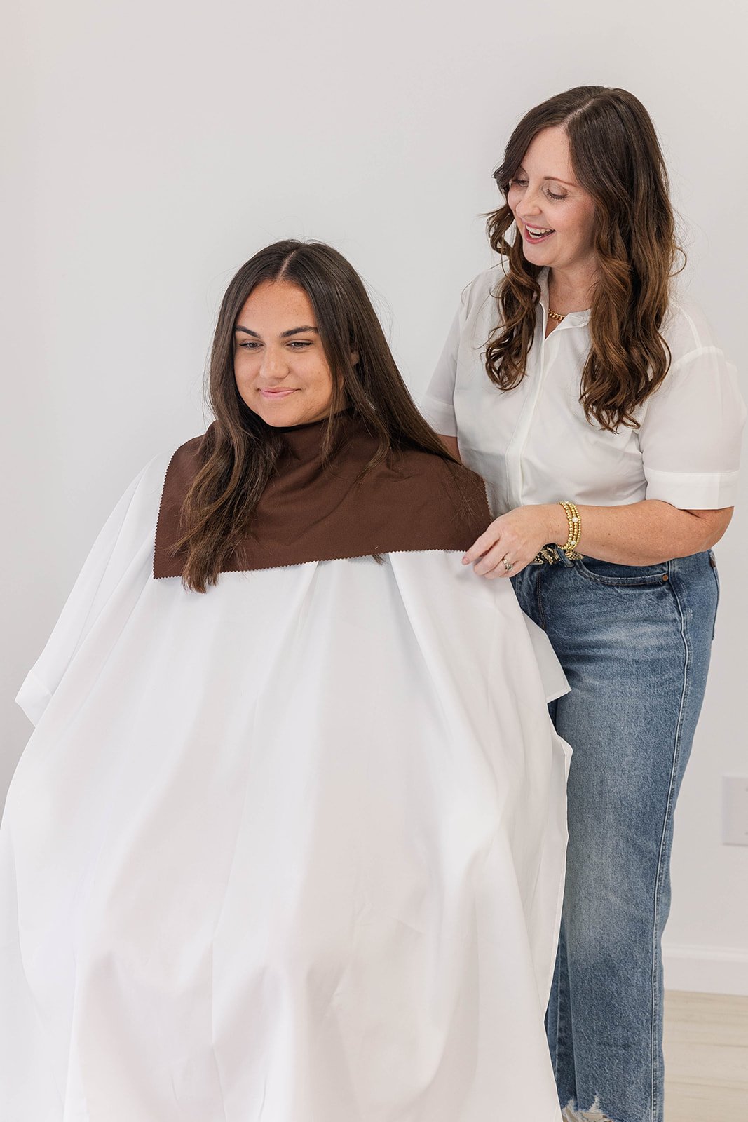 A woman sitting in a chair getting her hair styled by another woman.