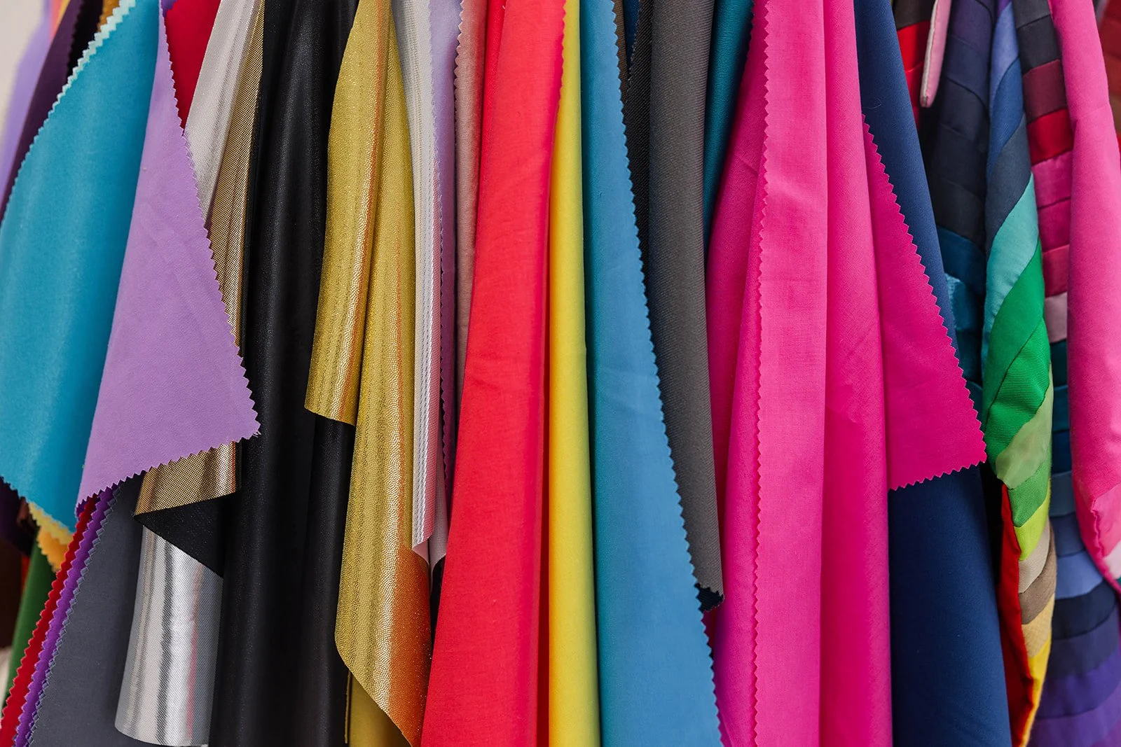 Colorful fabric swatches hanging on a rack, including pink, blue, yellow, black, purple, gold, and striped patterns.