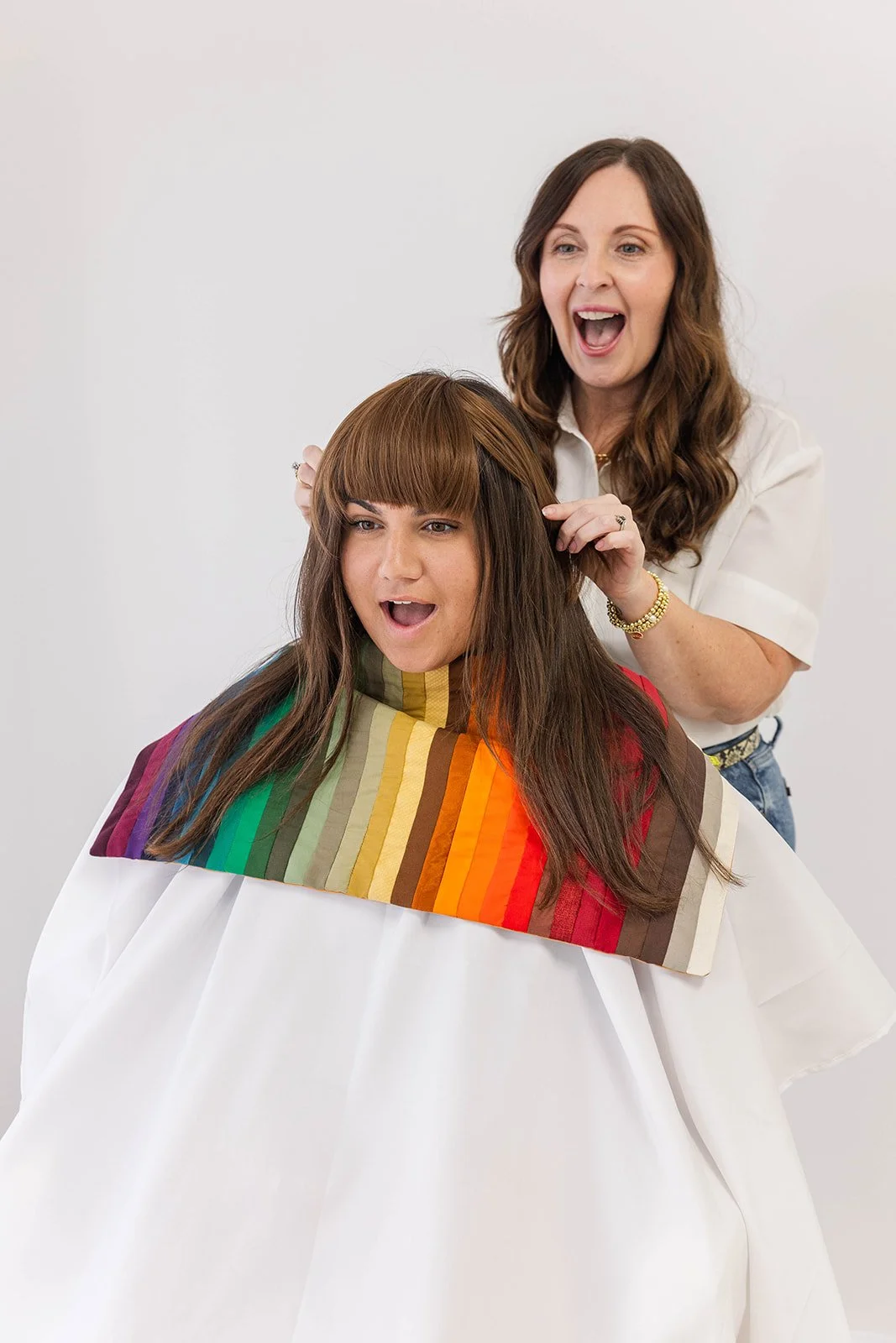 A woman at a hair salon getting a haircut from a stylist, with the stylist smiling and the client looking surprised.