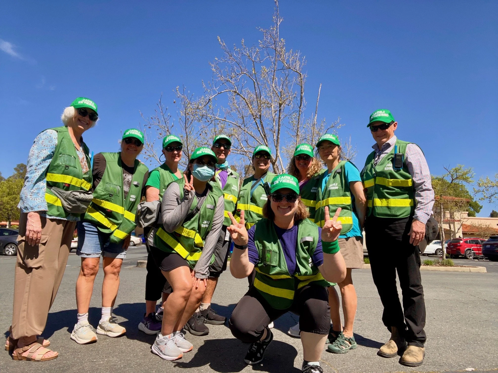 A group poses on a city street, wearing legal observer vests and hats.