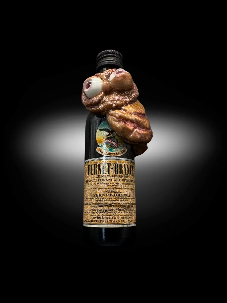 close up of handmade owl figurine with exaggerated eyes on small alcohol bottle