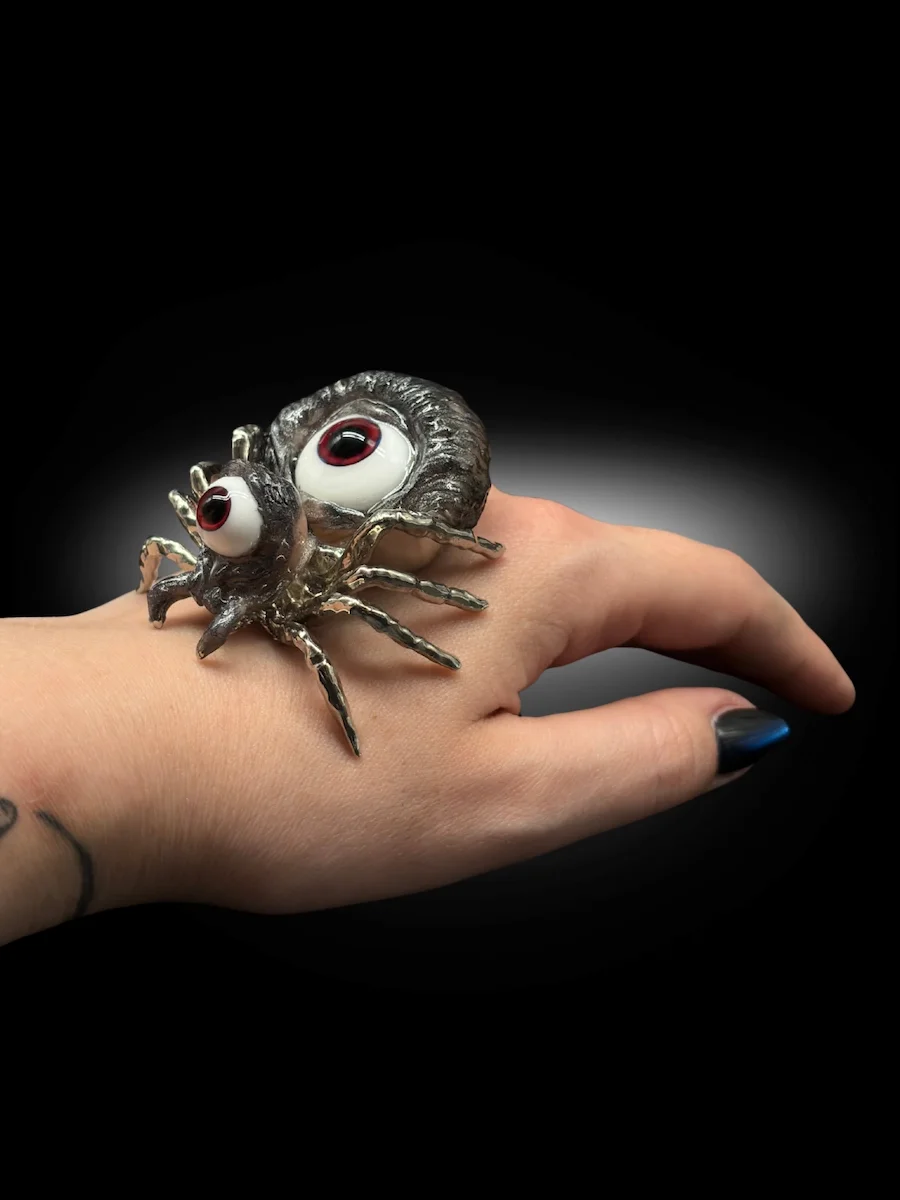 hand holding surreal spider sculpture with glass eyes and metallic legs