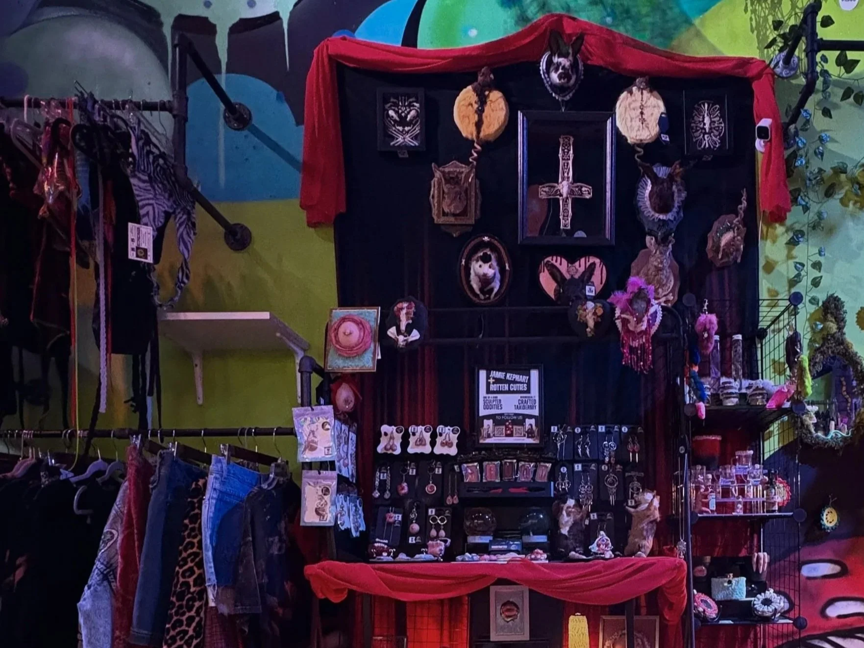 Display of jewelry, accessories, and decorative art on a shop wall with a Halloween or gothic theme.
