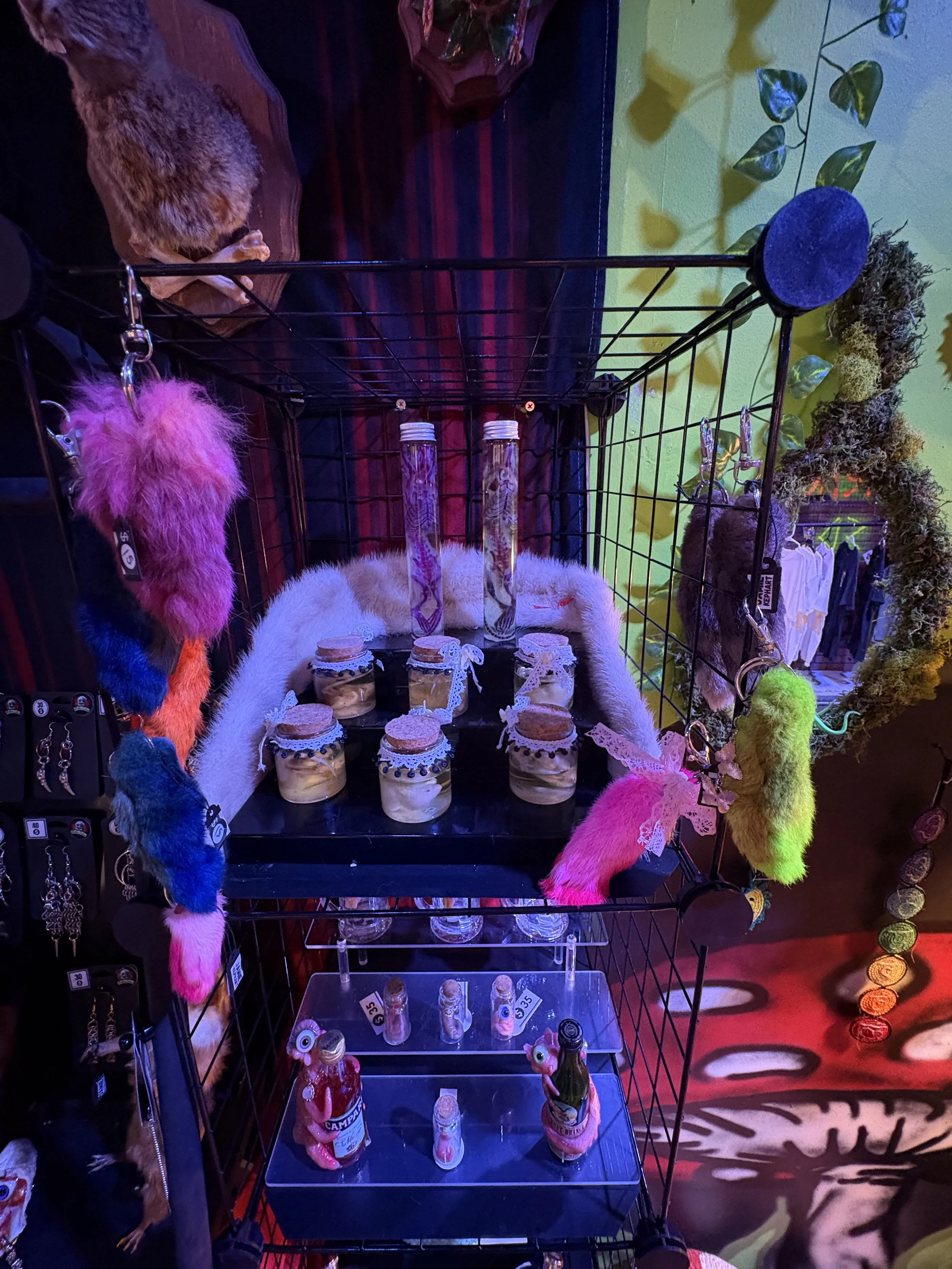A black metal display rack with colorful fuzzy keychains, small jars with decorations, and tall glass tubes with designs inside.