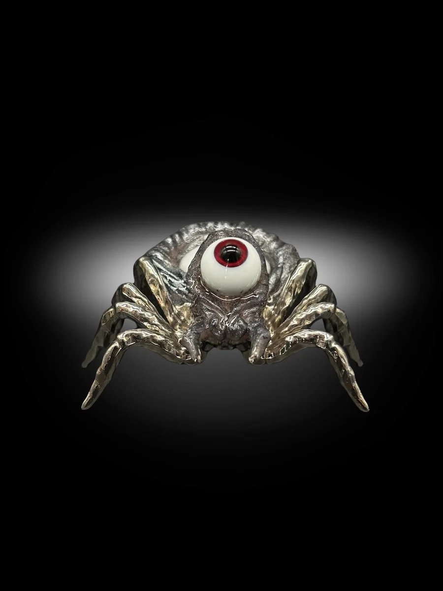 hand holding surreal spider sculpture with glass eyes and metallic legs