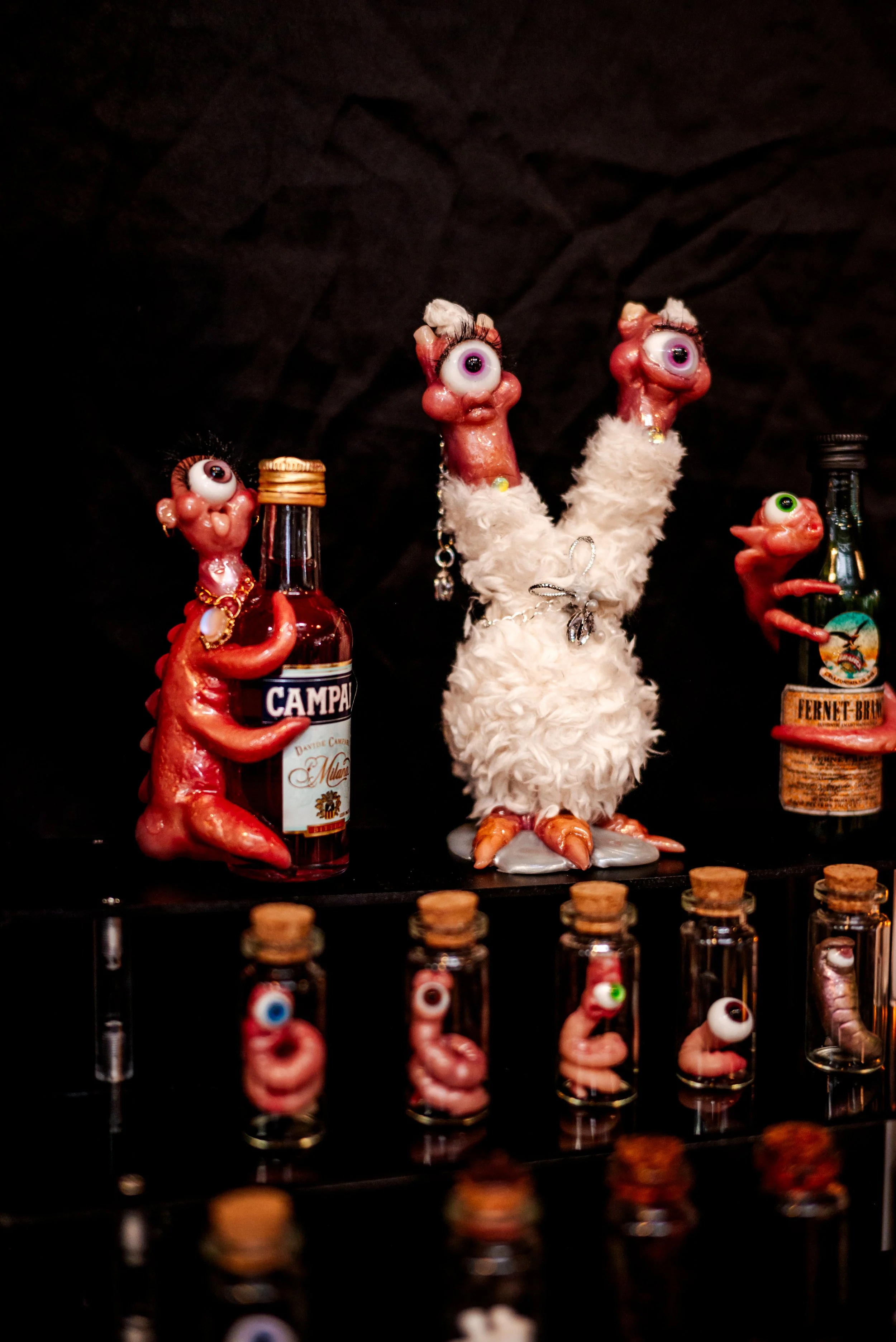 Decorative figurines with exaggerated eyes resembling caricatured characters, some holding bottles, displayed on a shelf with a dark background.