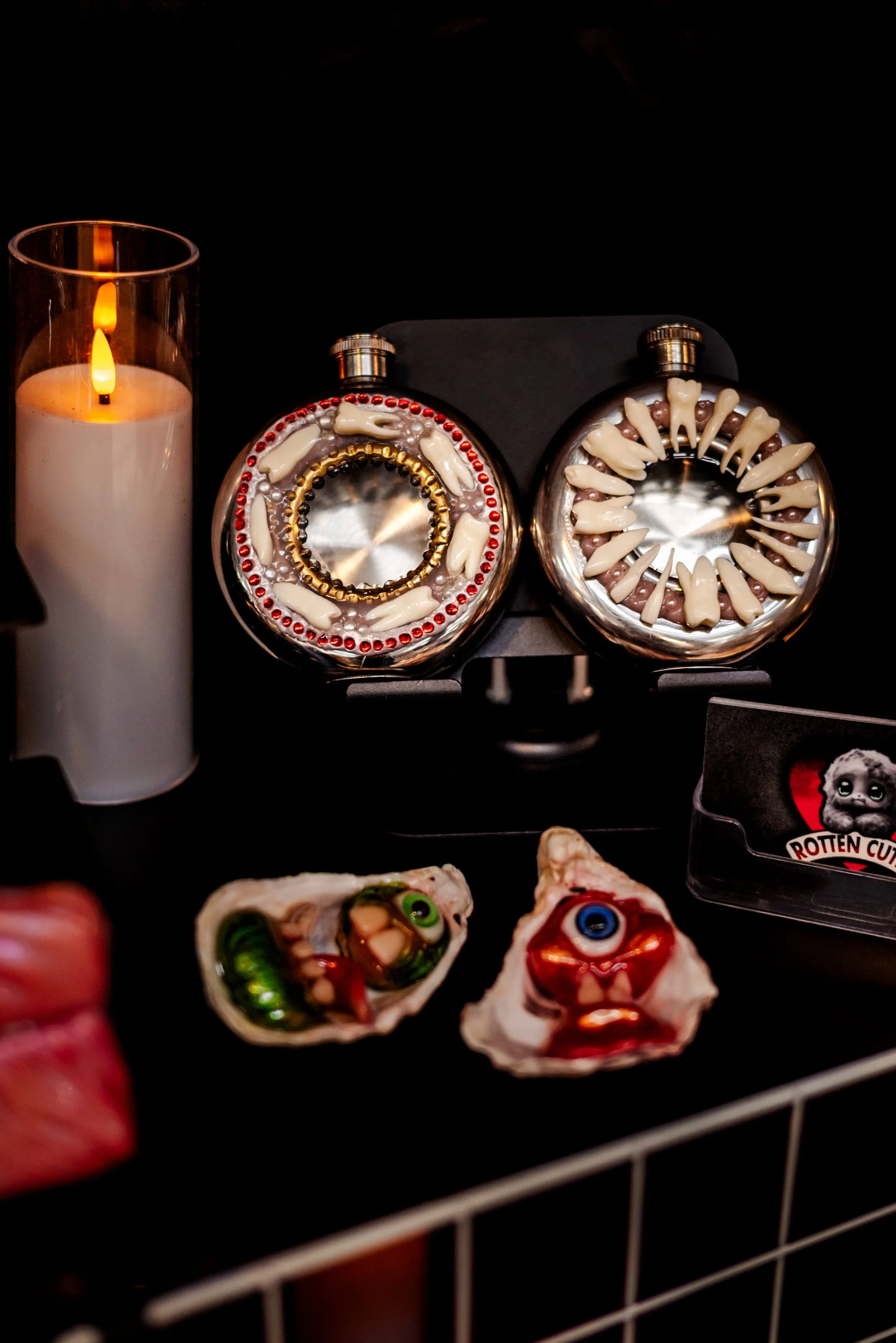 A candle, two decorative skulls with eyes, and two horror-themed perfume bottles in a dark setting.