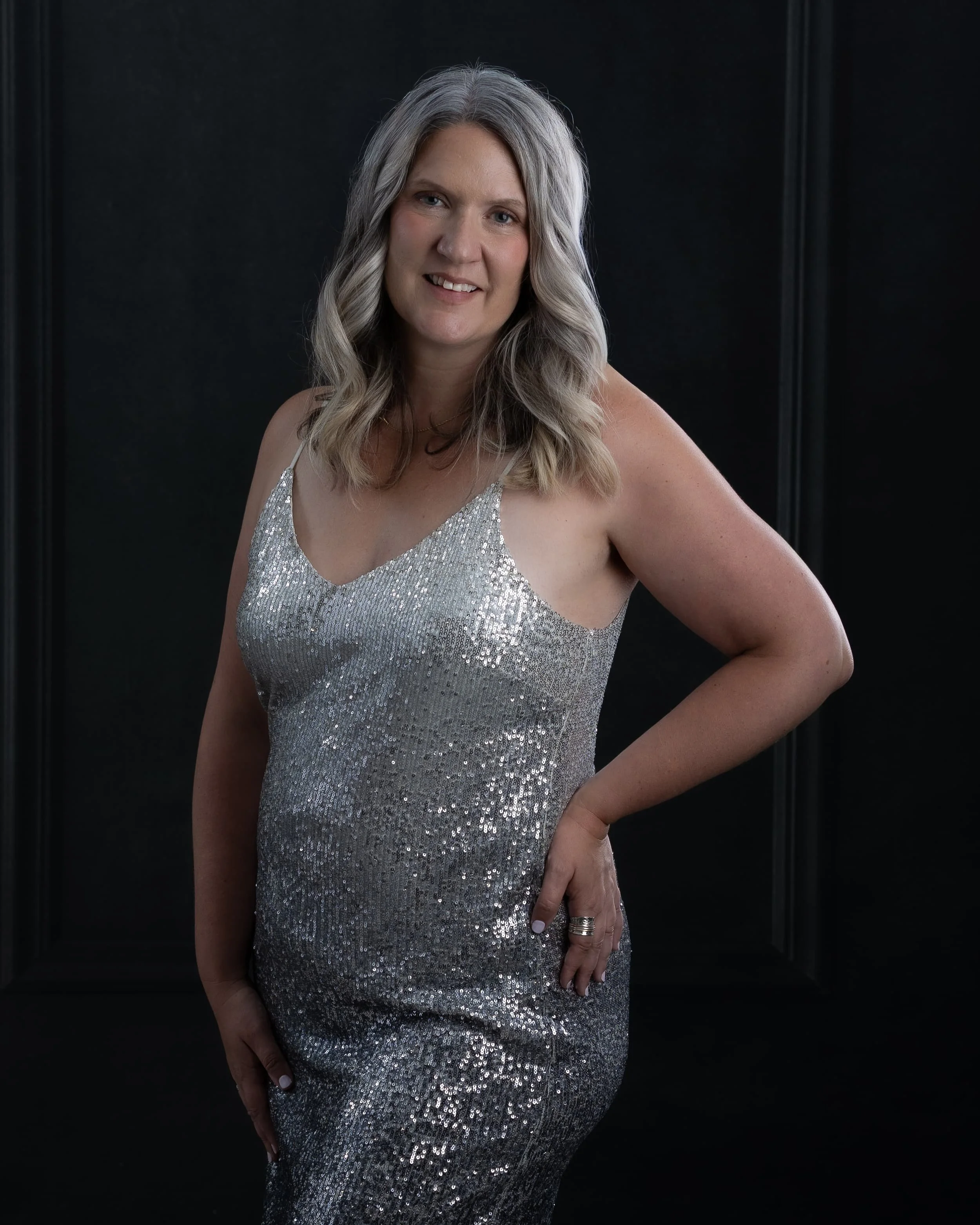 Woman wearing a silver sequin dress standing against a dark background.