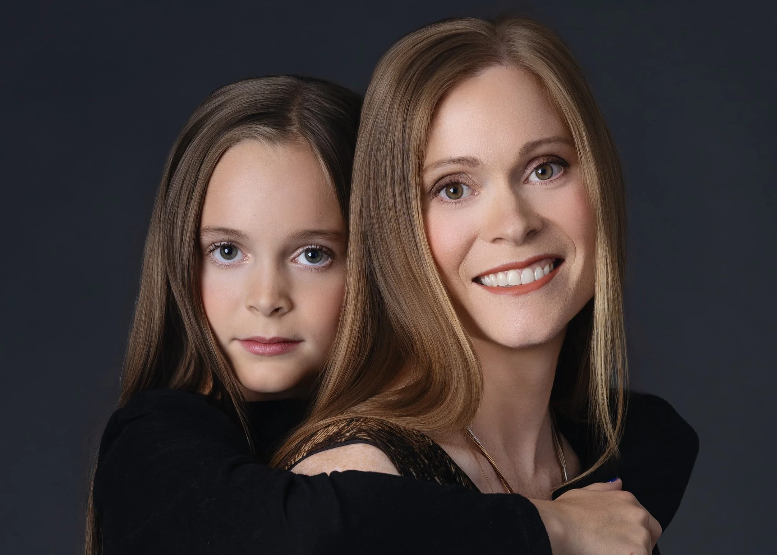 Cowichan valley Best photographer Beauty Portrait Mother and daughter A woman and a girl with light skin and long hair pose together against a dark background. The woman is smiling and the girl has a neutral expression.