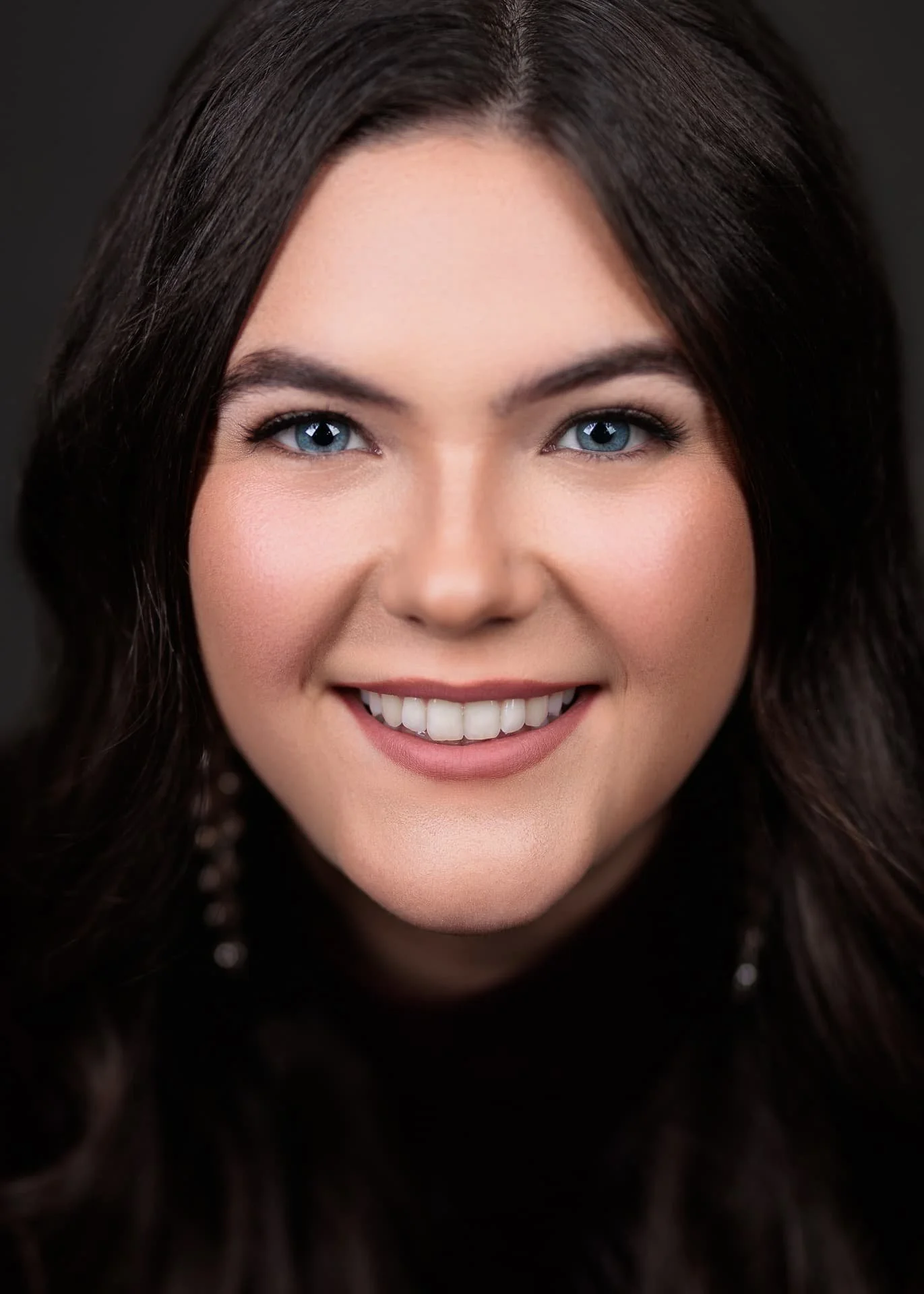 Cowichan valley Close-up portrait of a beautiful woman with long dark hair, blue eyes, and light makeup, against a dark background. Opera singer Soprano Headshop
