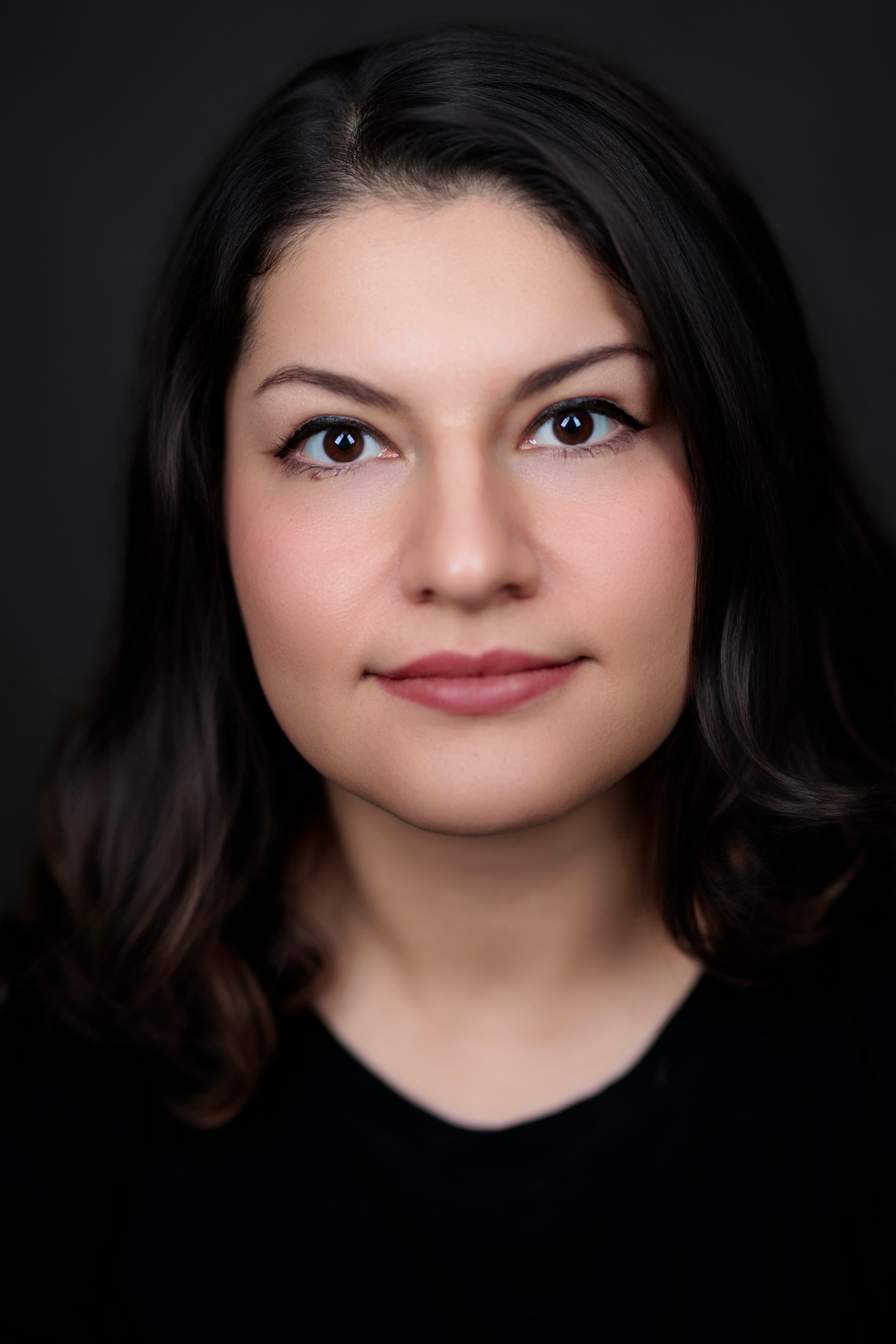 Glenn Mathieson Best Photographer in DuncanClose-up portrait of a young woman with dark brown hair and brown eyes, wearing a black top, against a dark background.