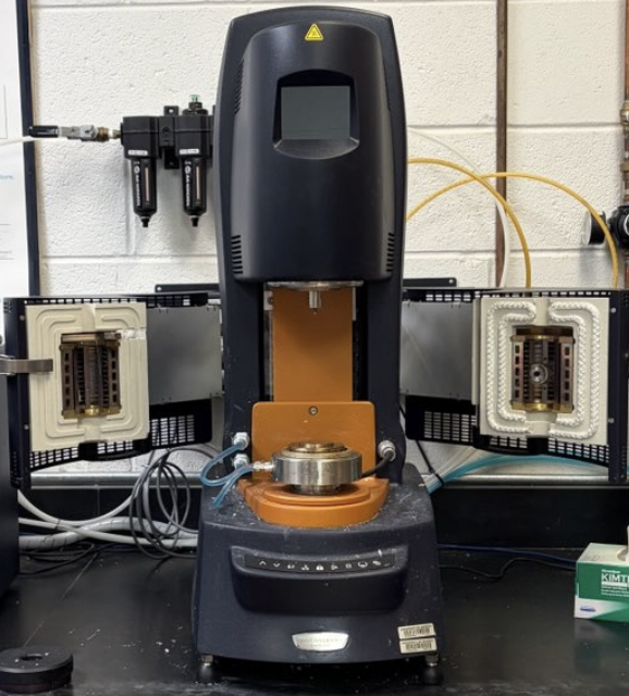 A mechanical testing machine with a central movable arm, surrounded by electrical connections and wiring.