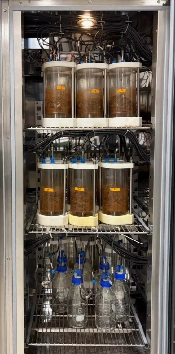 Laboratory equipment with multiple glass containers connected by tubes and wires inside a metal cabinet.