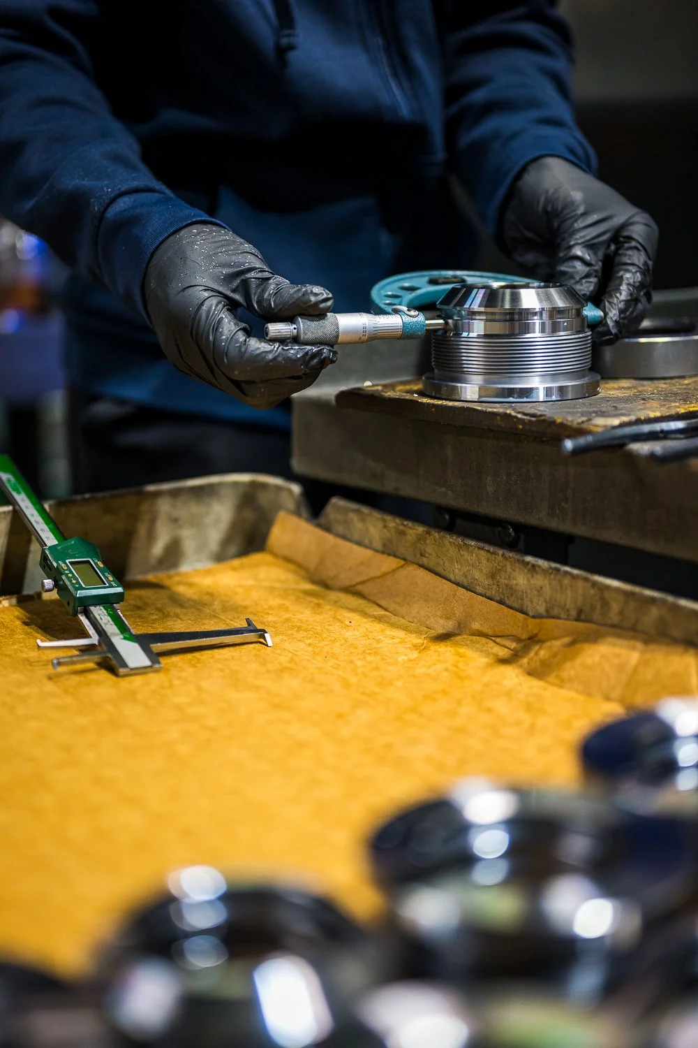 A person in black gloves using a micrometer to measure a hydraulic component.