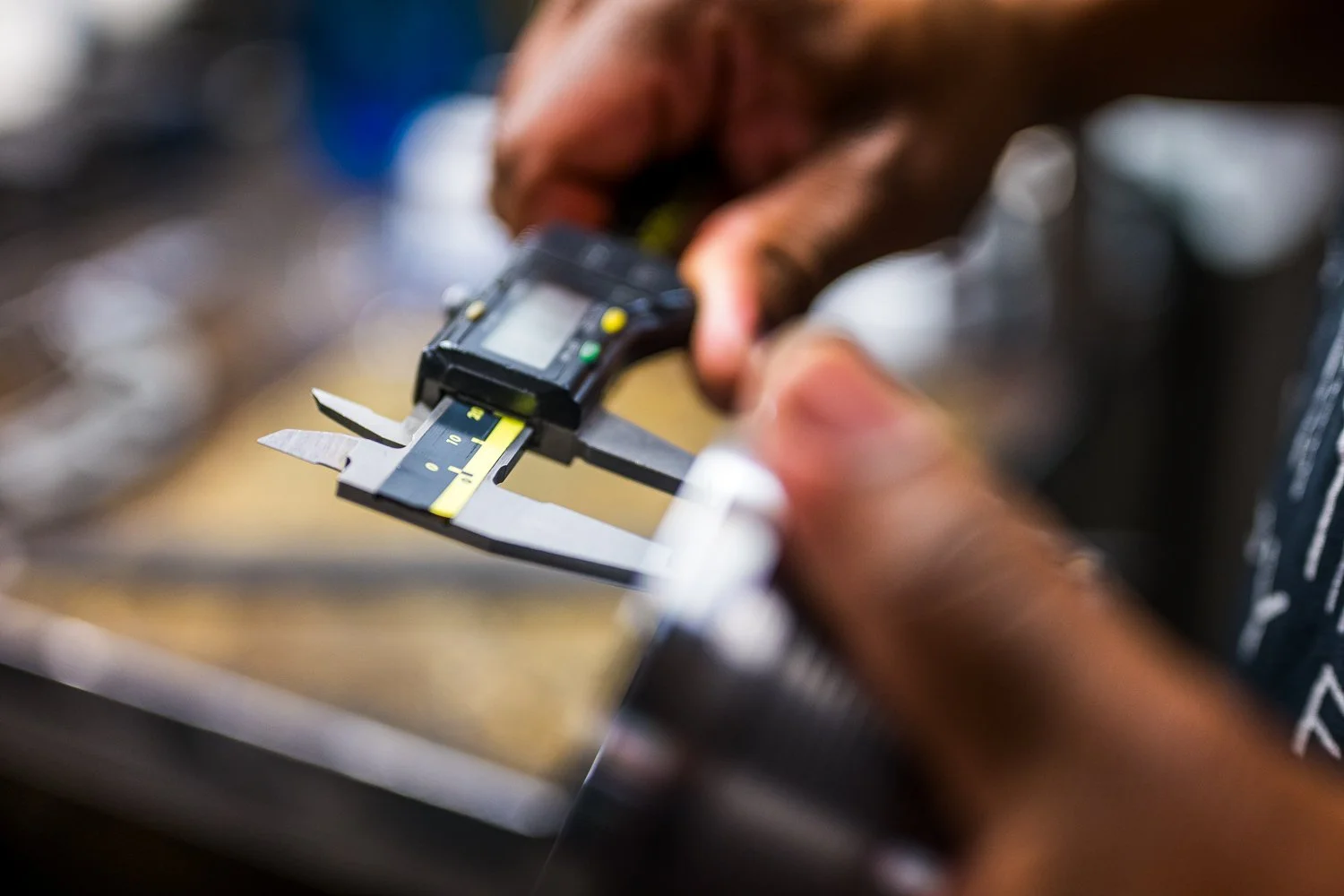 Close-up of a person measuring a manufactured part with a digital caliper in a workshop.