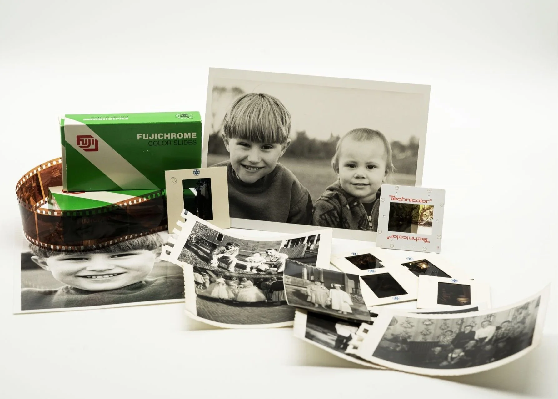 Collection of black and white photographs, film strip, and slide frames surrounding a large printed photo of two young boys smiling.