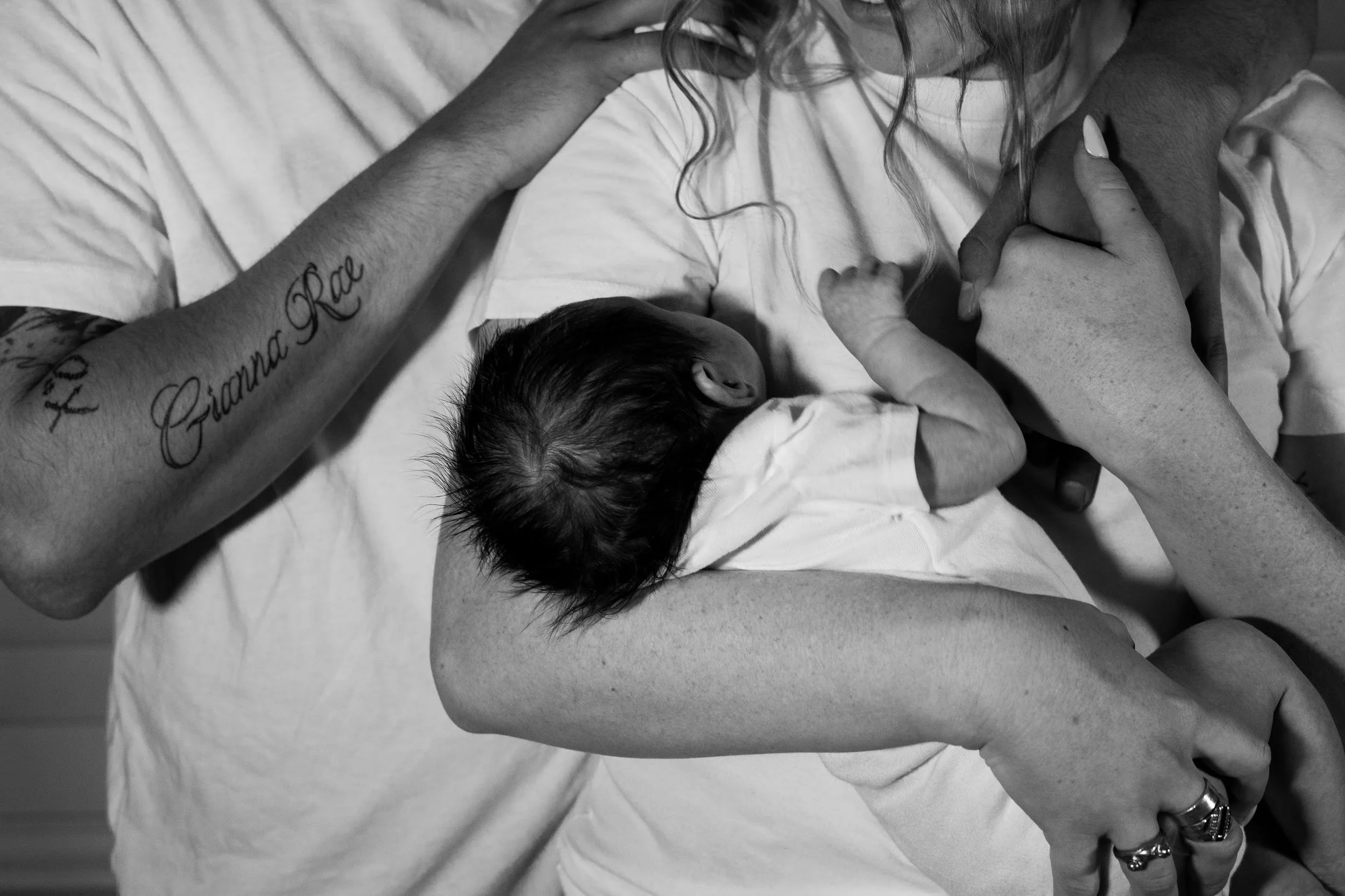 A newborn baby resting on a woman's chest, with another person supporting and holding the woman, in black and white.