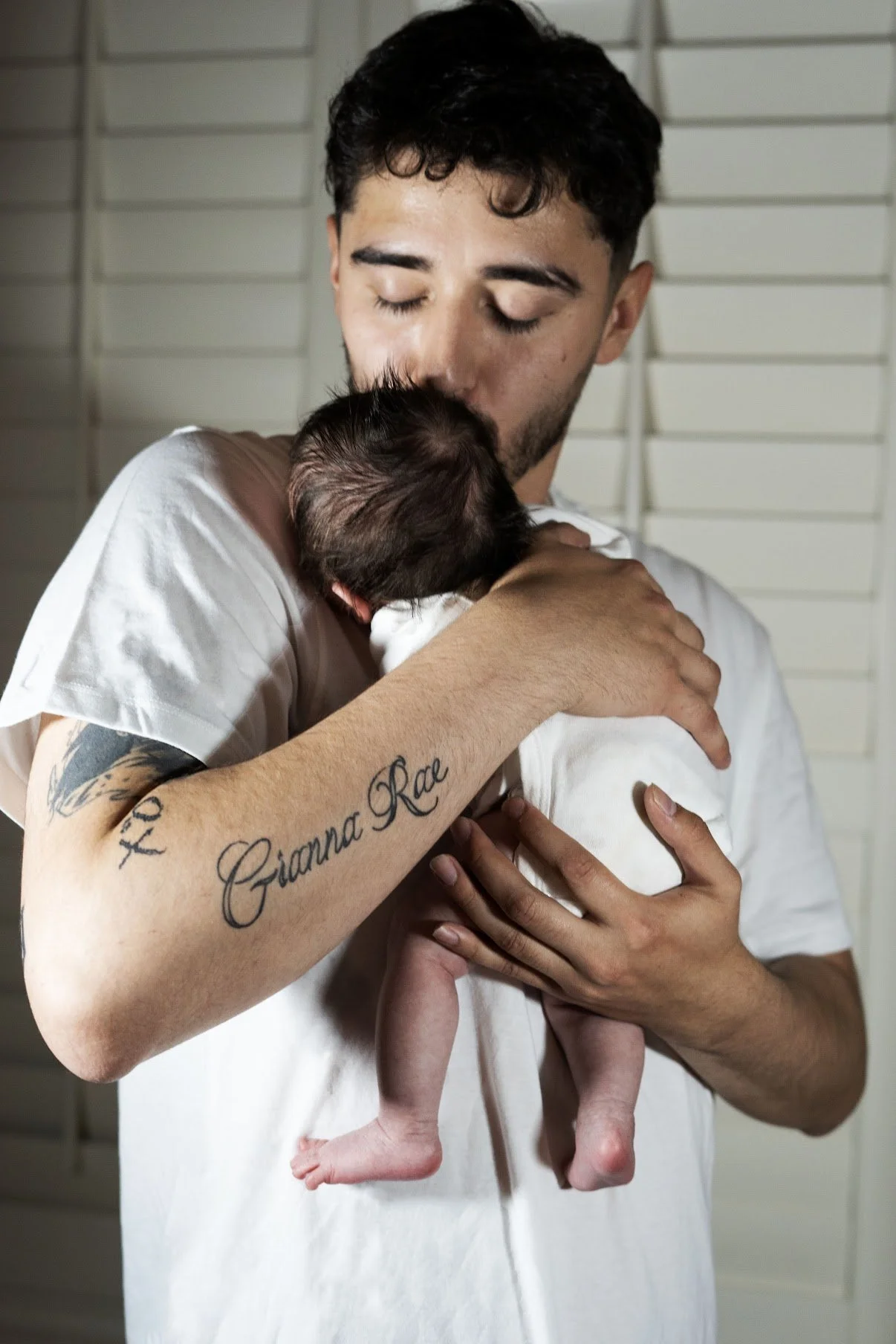 A man holding a newborn baby close to his chest, gently kissing the baby's head.