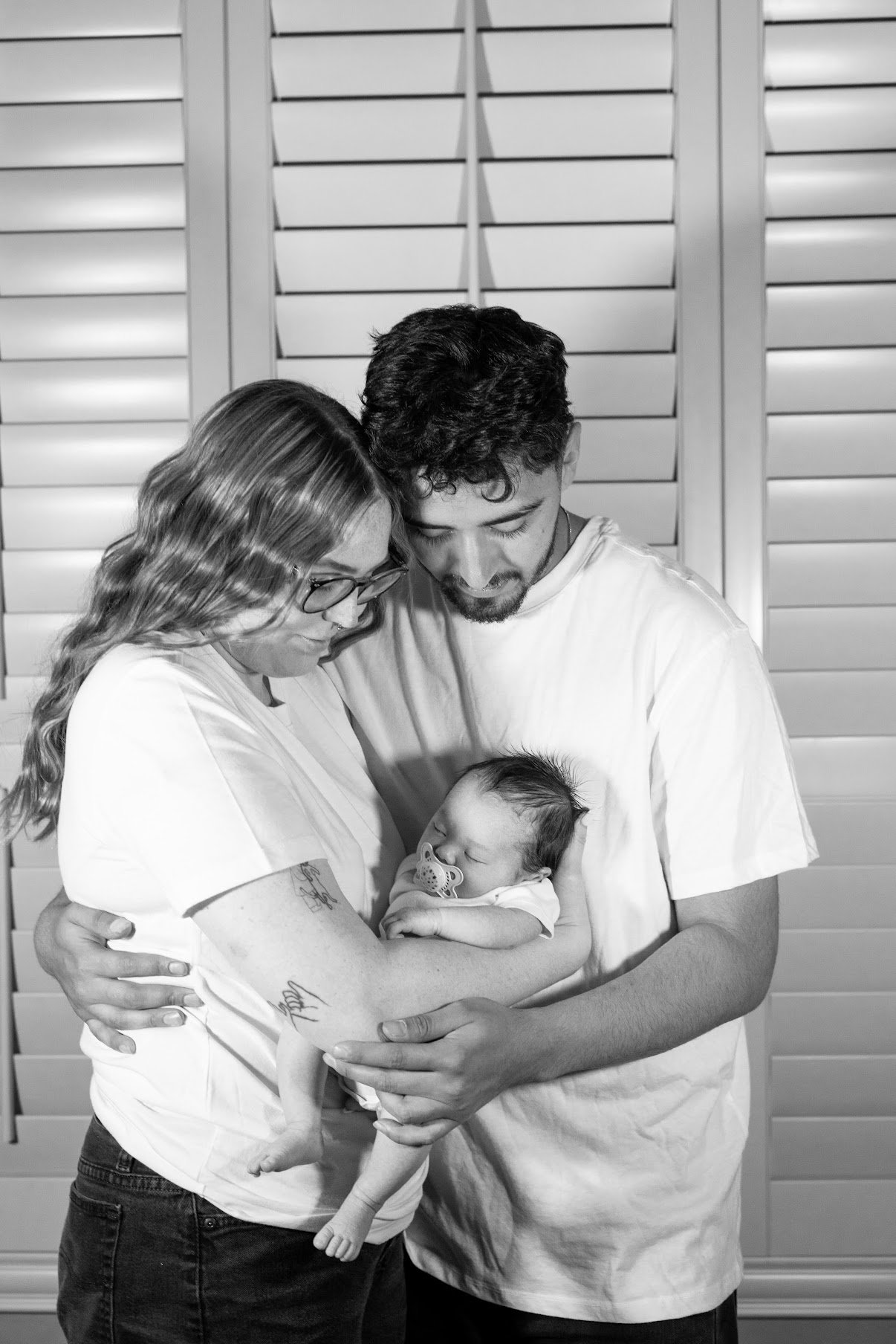 A black and white photo of a family holding a newborn baby, with the parents looking at the baby affectionately.