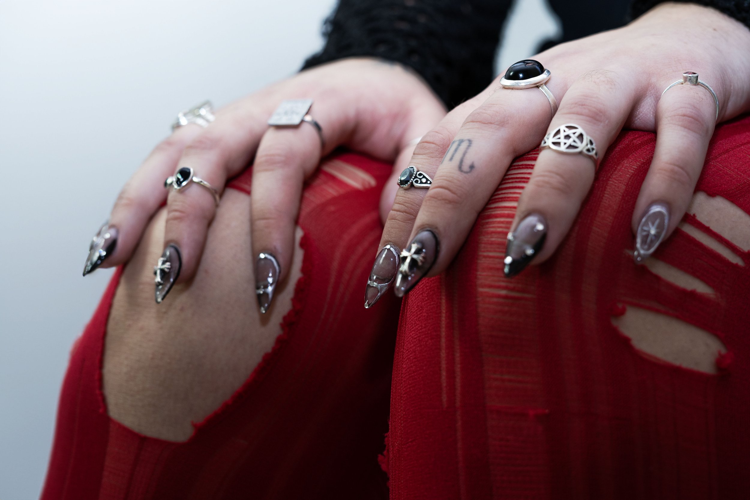 Close-up of a person's hands with multiple rings and painted nails, resting on a red, distressed fabric garment.