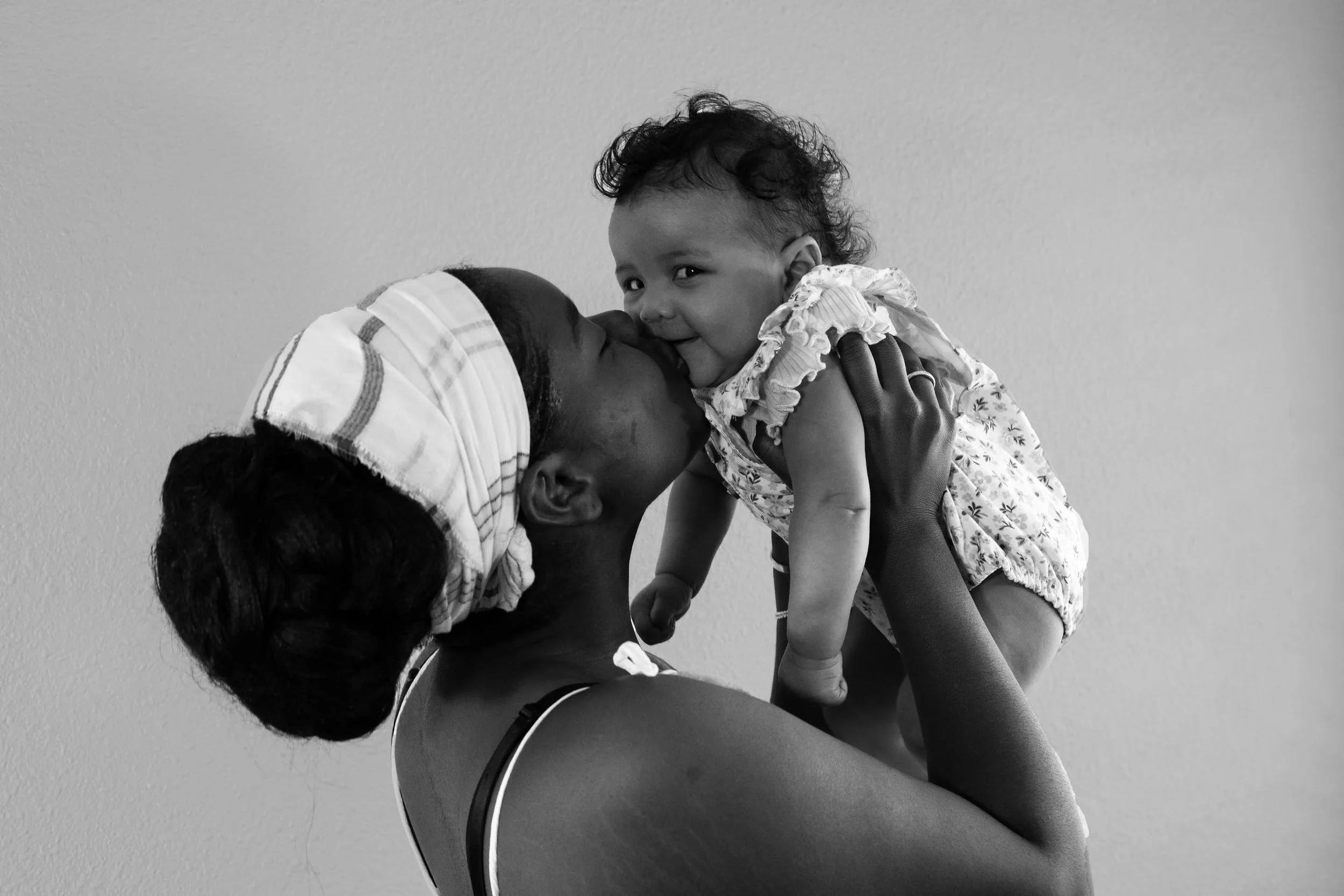 A woman is holding a young girl close, and they are about to kiss or touch noses, both smiling. The image is in black and white.