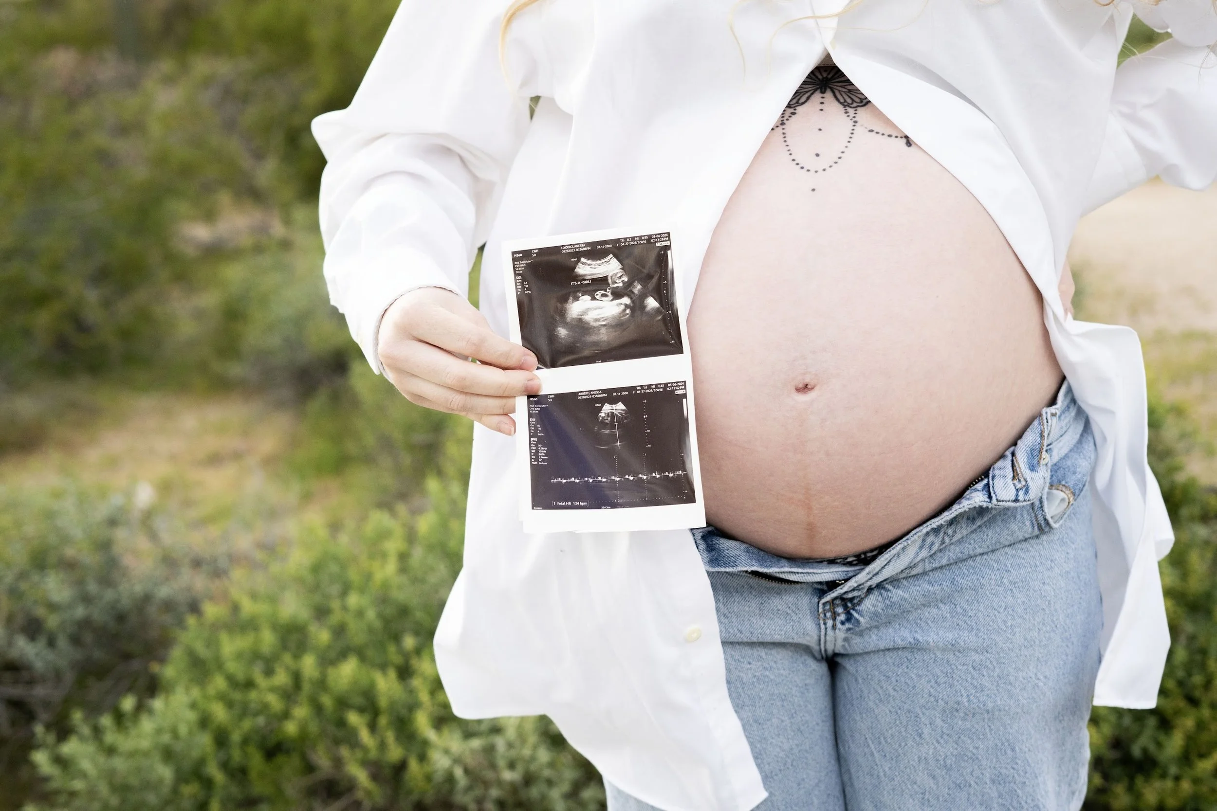 Pregnant woman outdoors showing ultrasound images of her pregnancy.