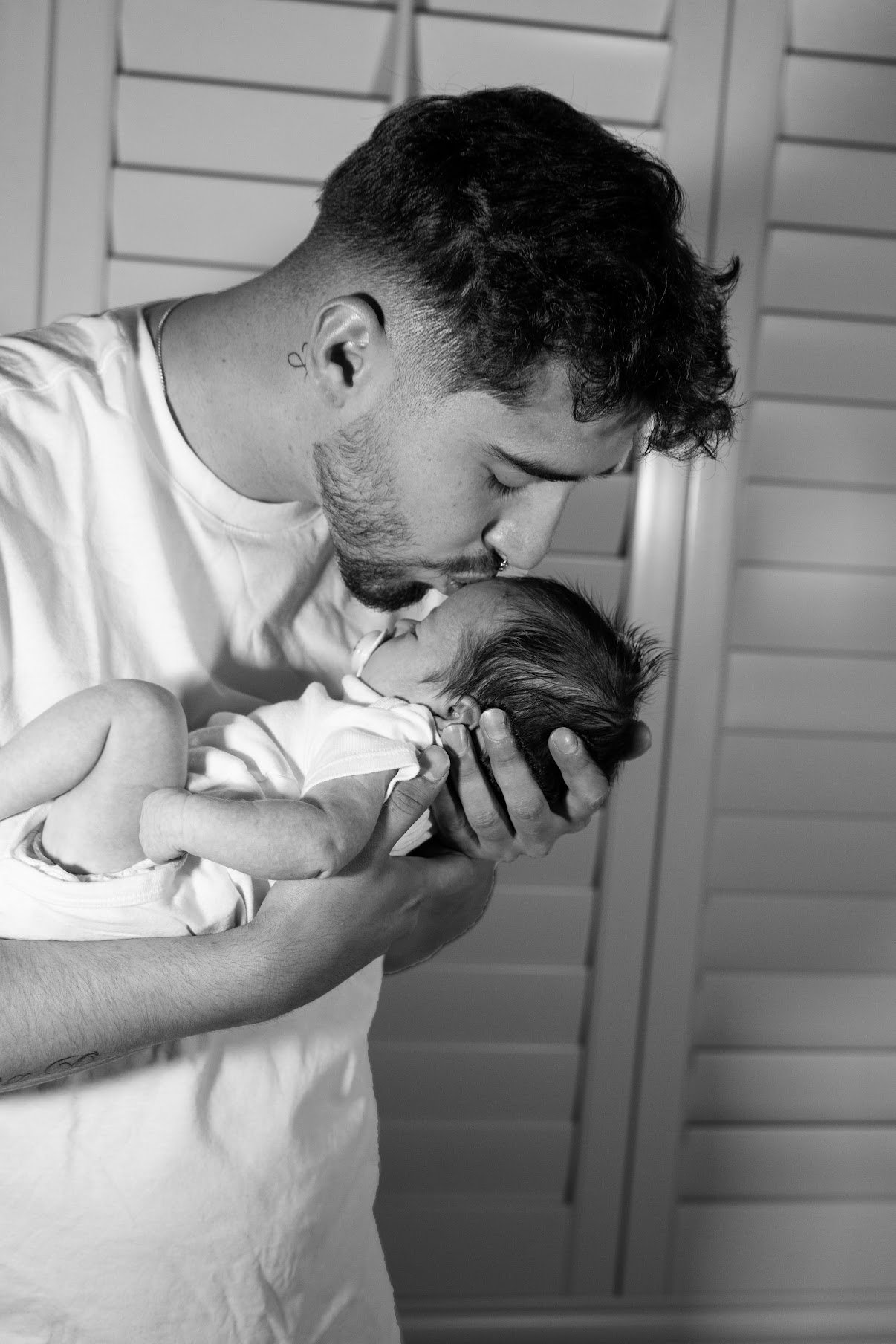 A man gently holding and kissing a newborn baby near his face.