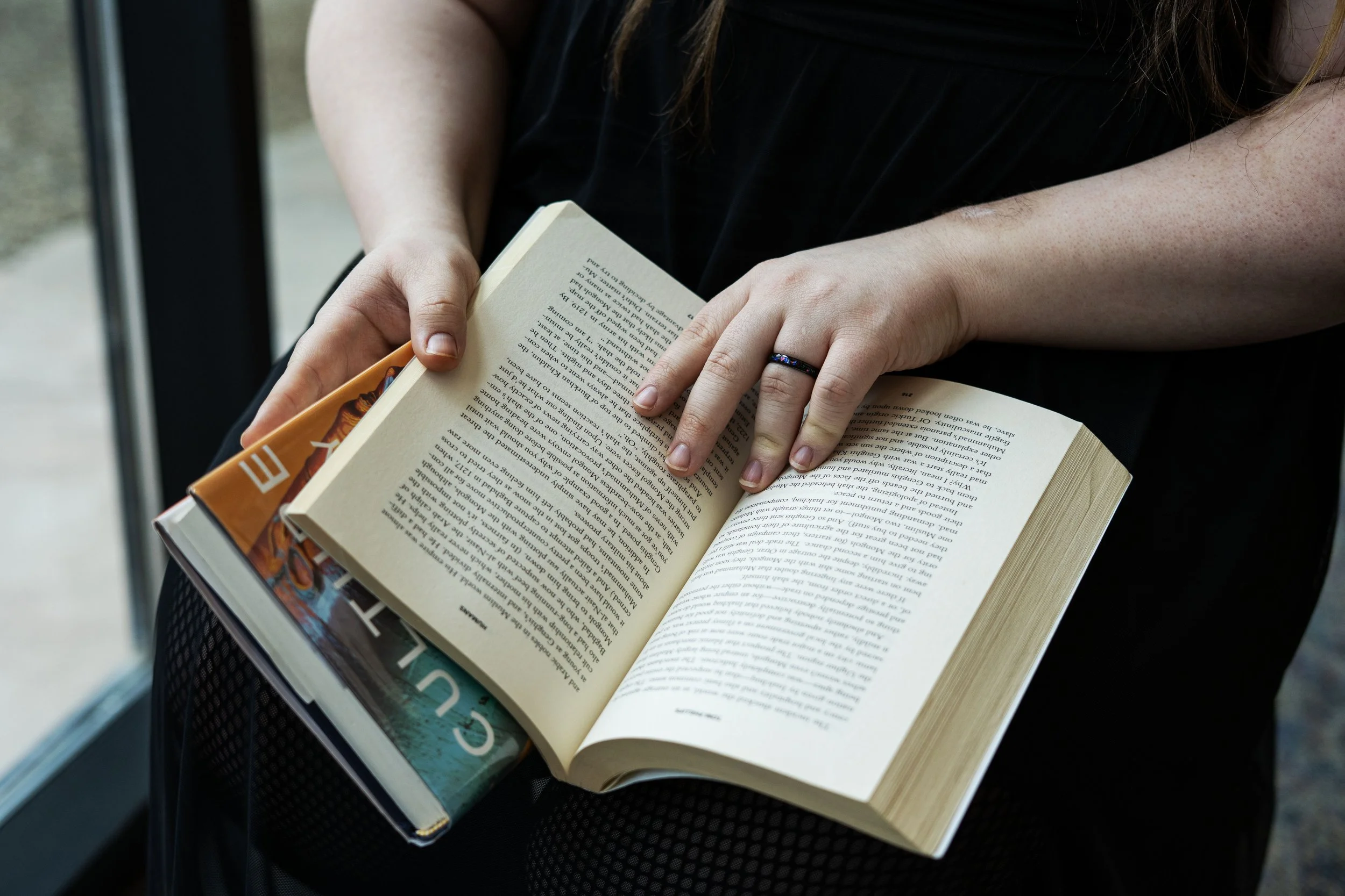 Person holding an open book and a magazine, sitting near a window.