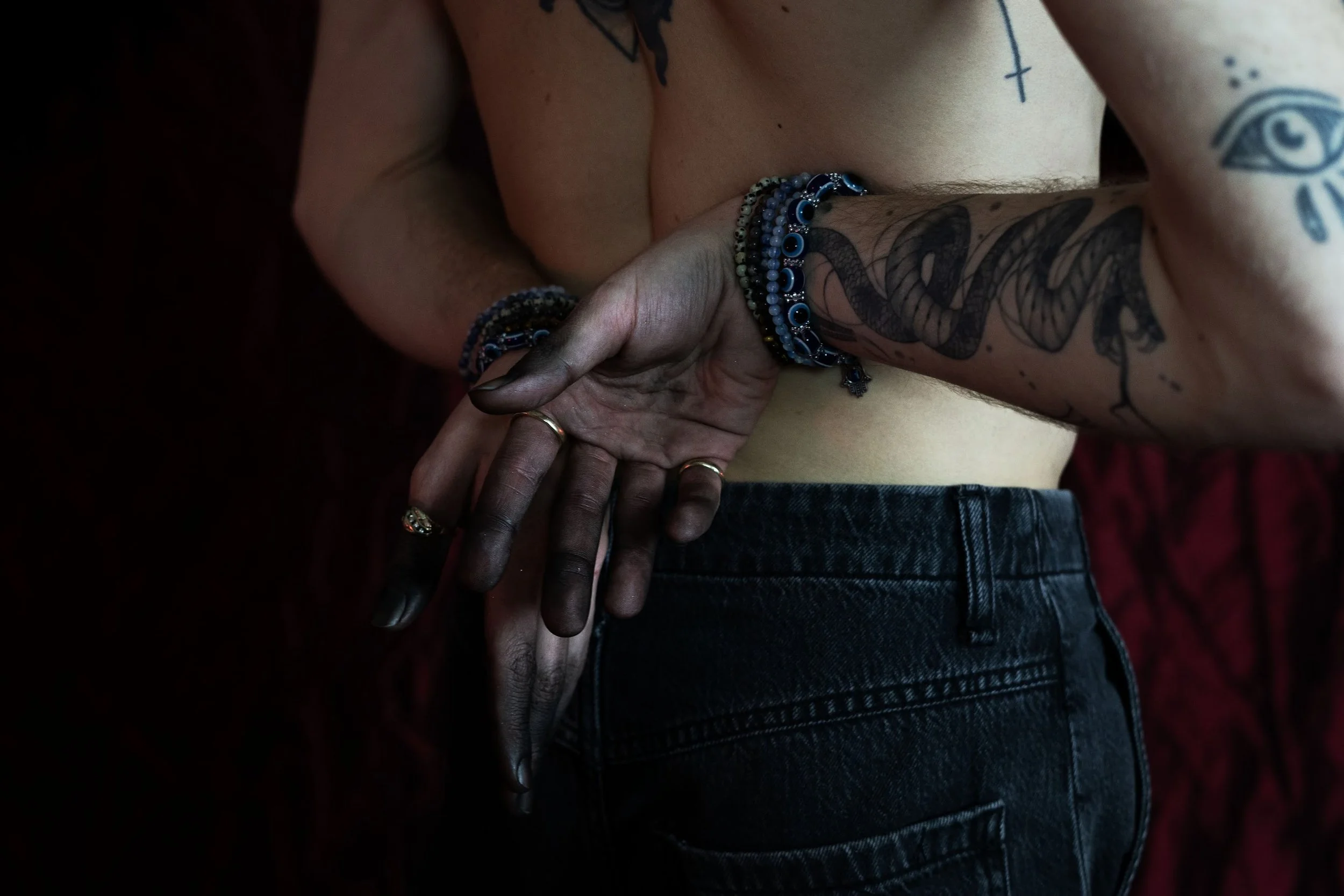 Close-up of a person with tattoos and multiple bracelets, touching another person's hand.
