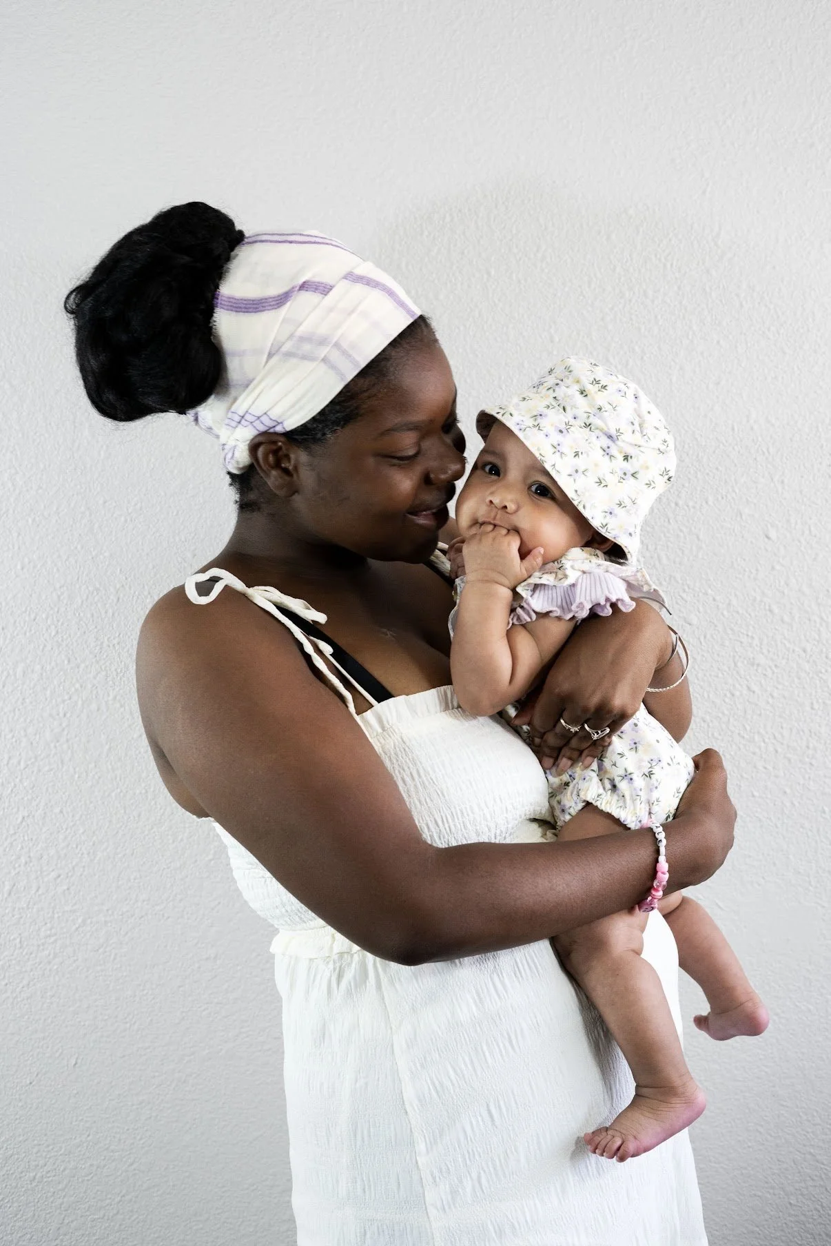 A woman holding a baby girl against a plain wall.