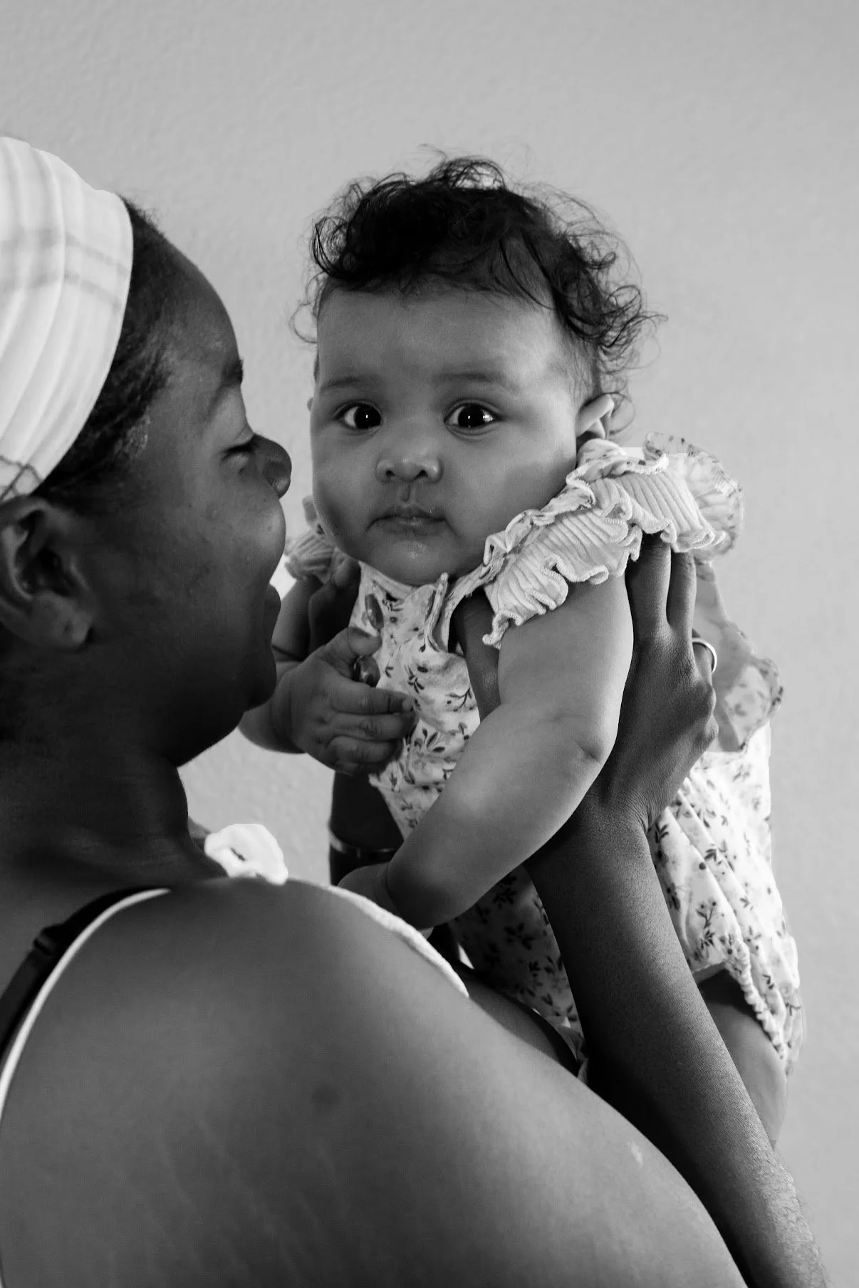 A woman holding a baby girl close to her face, both looking at each other, in a black and white photograph.