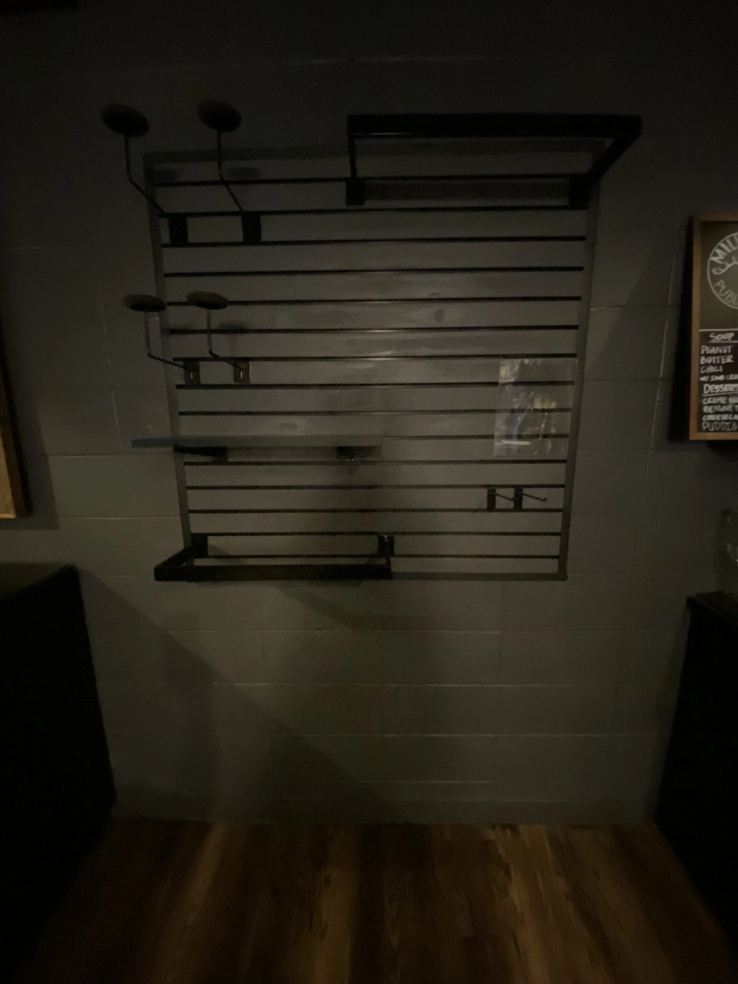 Empty wall-mounted metal slat rack on a tiled wall, with two small black wall hooks, in a dimly lit room.