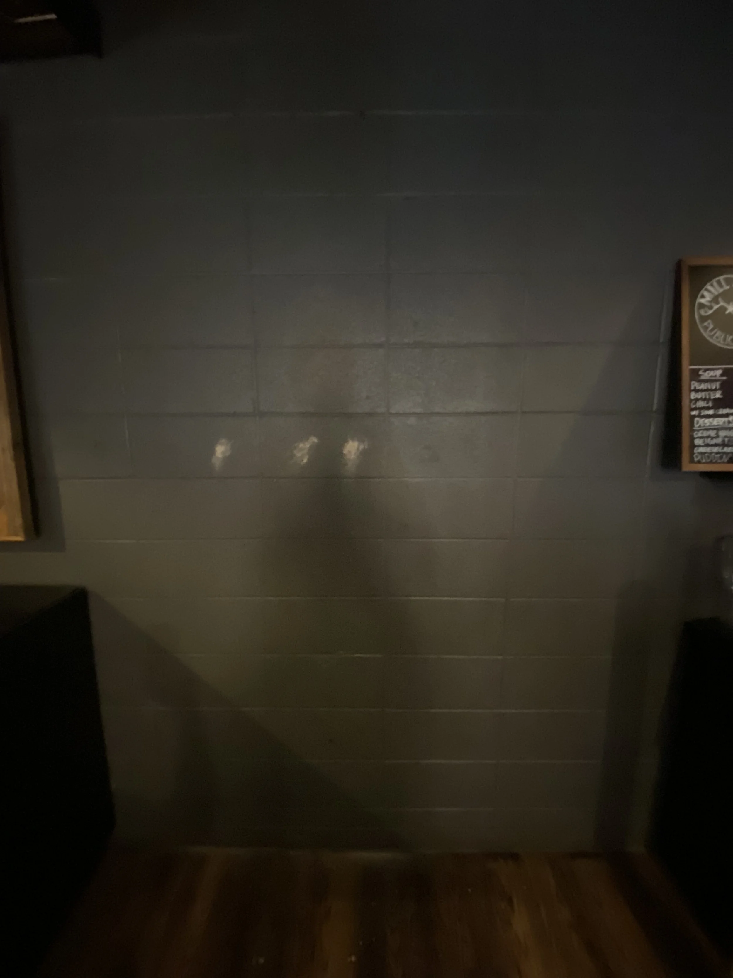 Dark-colored tiled wall with three white finger marks or scratches, partially illuminated with shadows.
