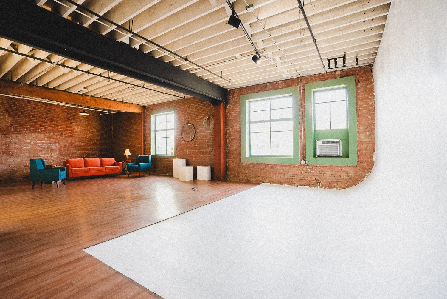Sunlit Santa Ana studio with exposed brick, hardwood floors, lounge seating and a white cyclorama