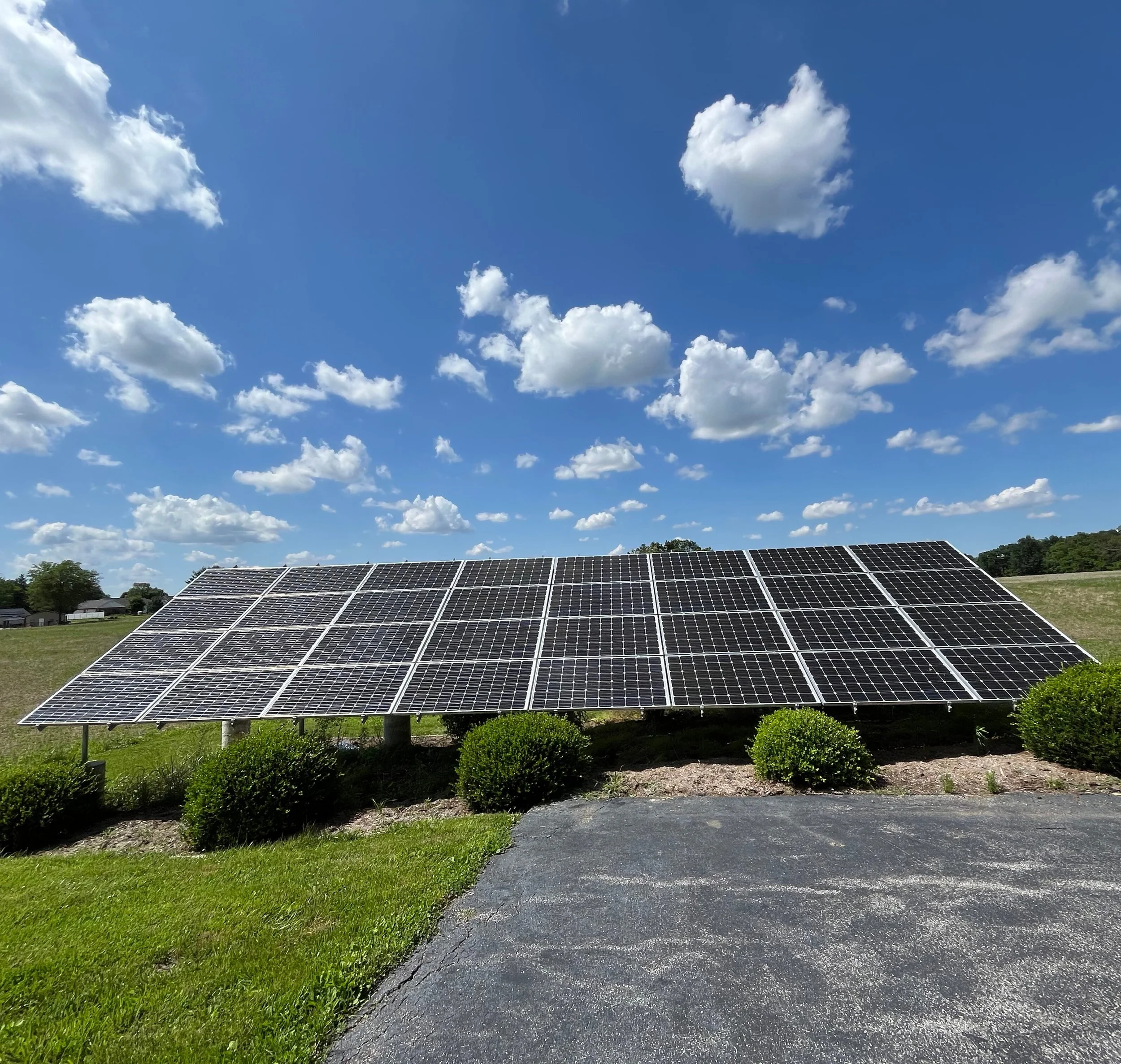 Solar panels on a grassy field under a blue sky with white clouds.